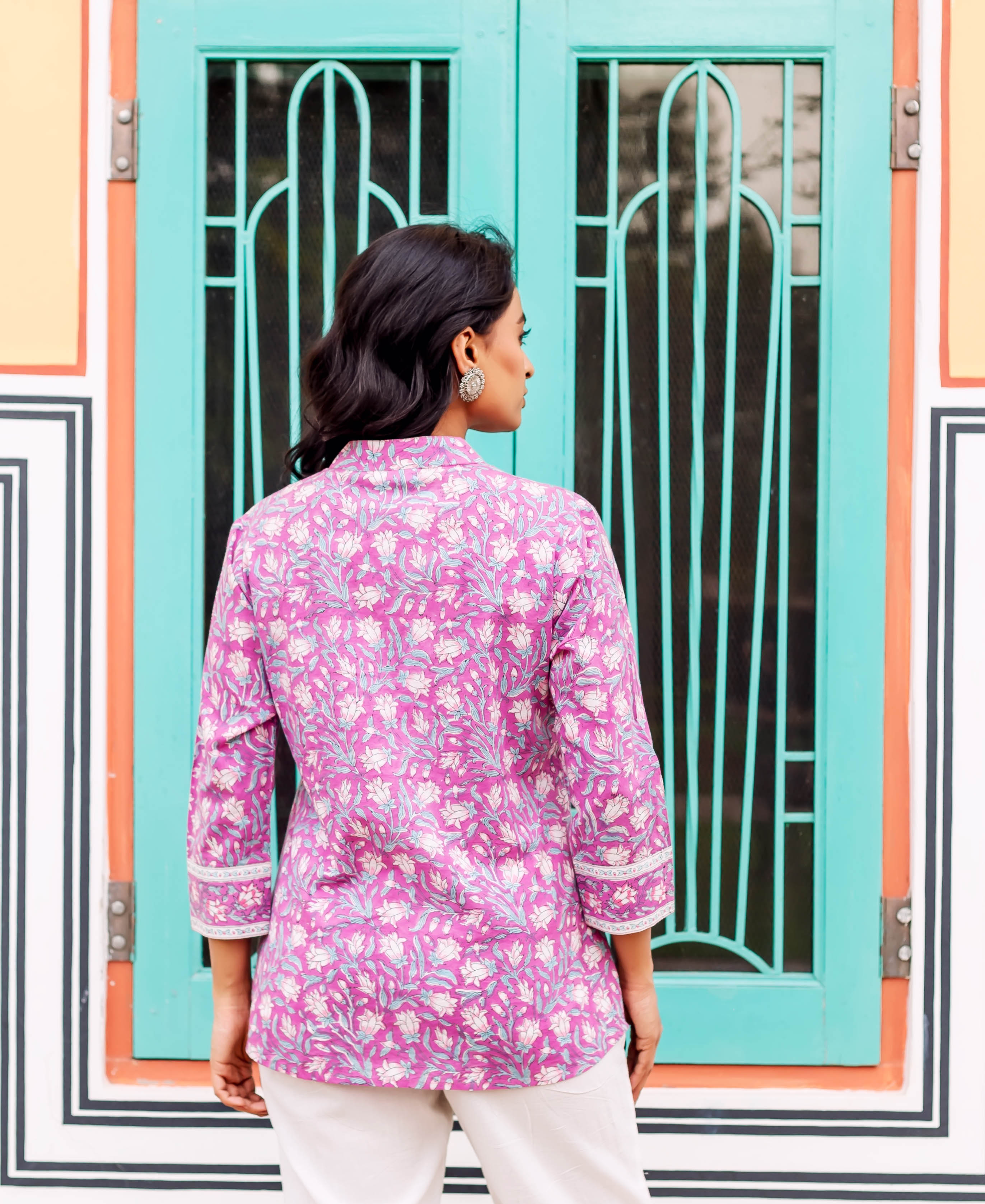 Back of model wearing a vibrant purple floral hand-block printed tunic with white pants.