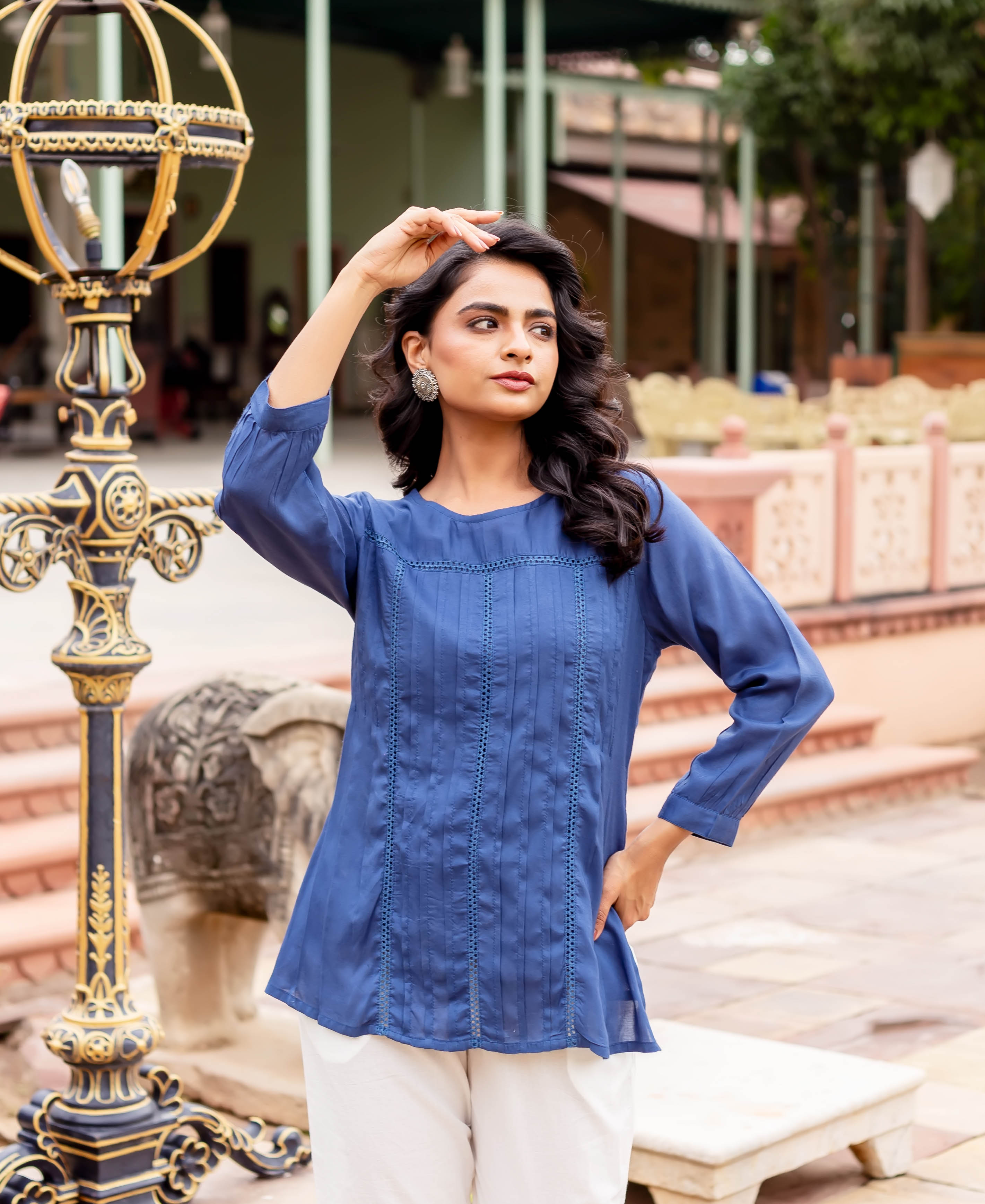 Model poses in a navy blue pleated tunic featuring front pintucks and eyelet lace inserts.