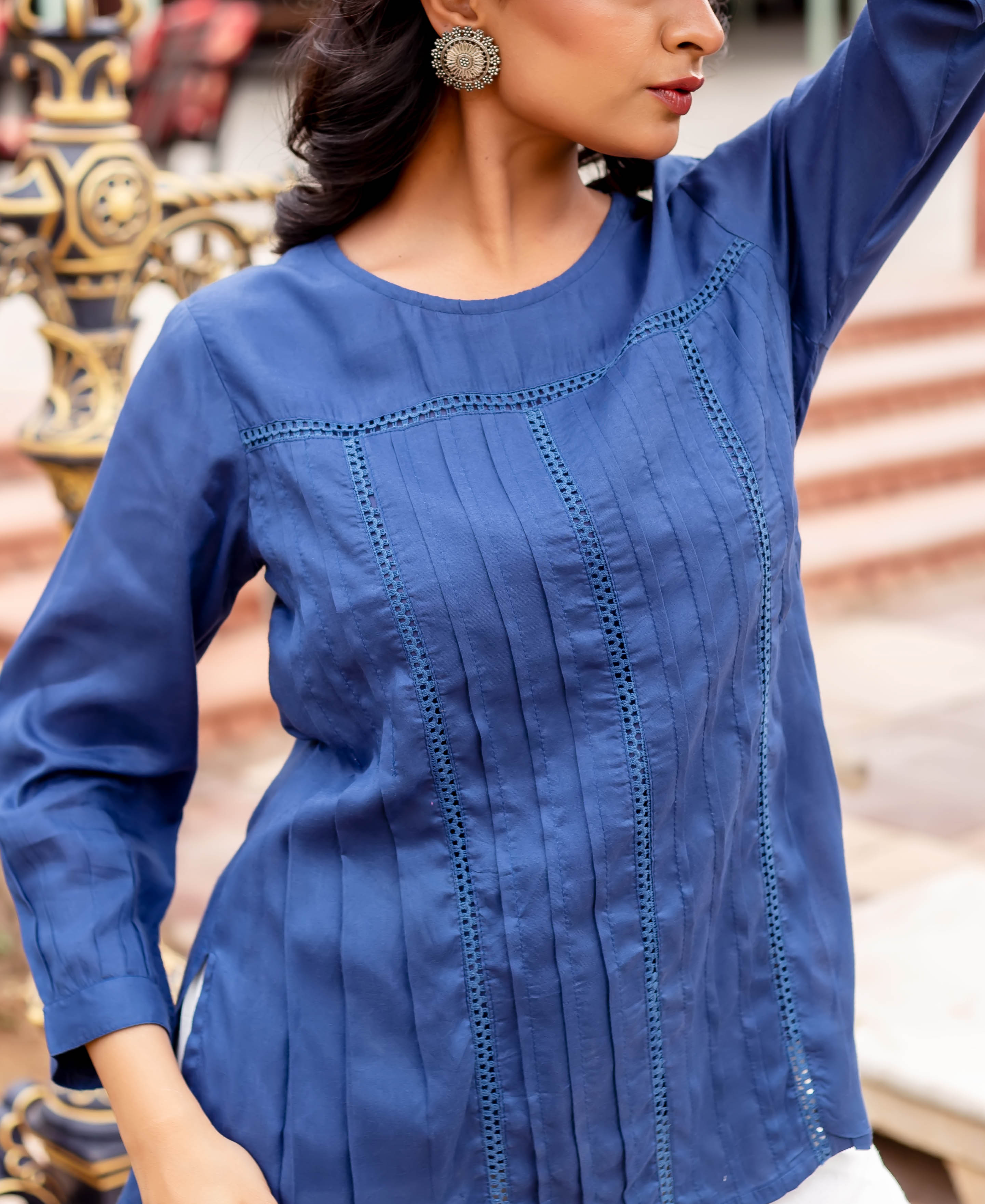 Model in a navy blue tunic, featuring extensive vertical pleats and intricate lace details.