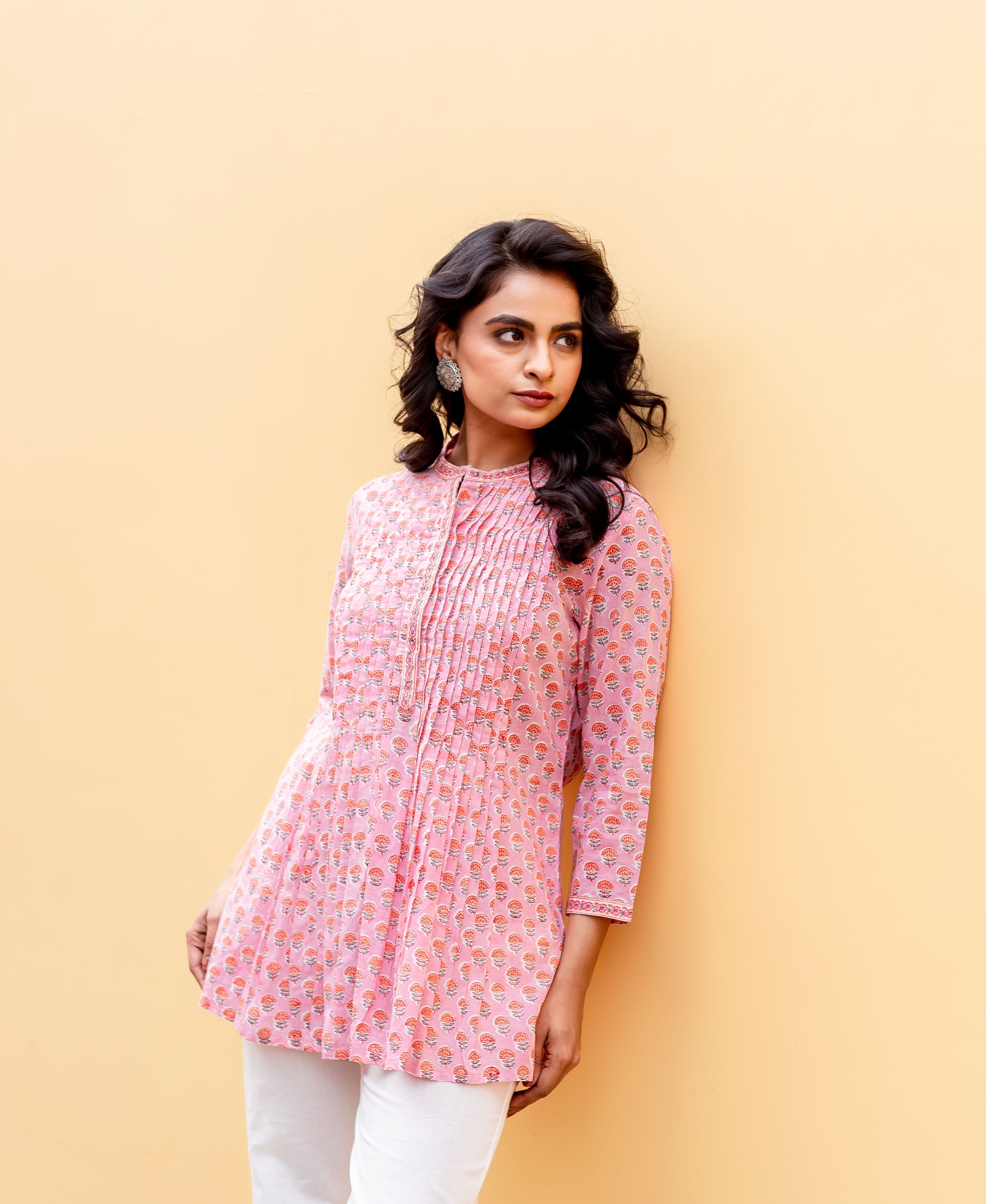 Model wears a blush pink hand-block-printed ethnic tunic with pintucks, against a yellow wall.