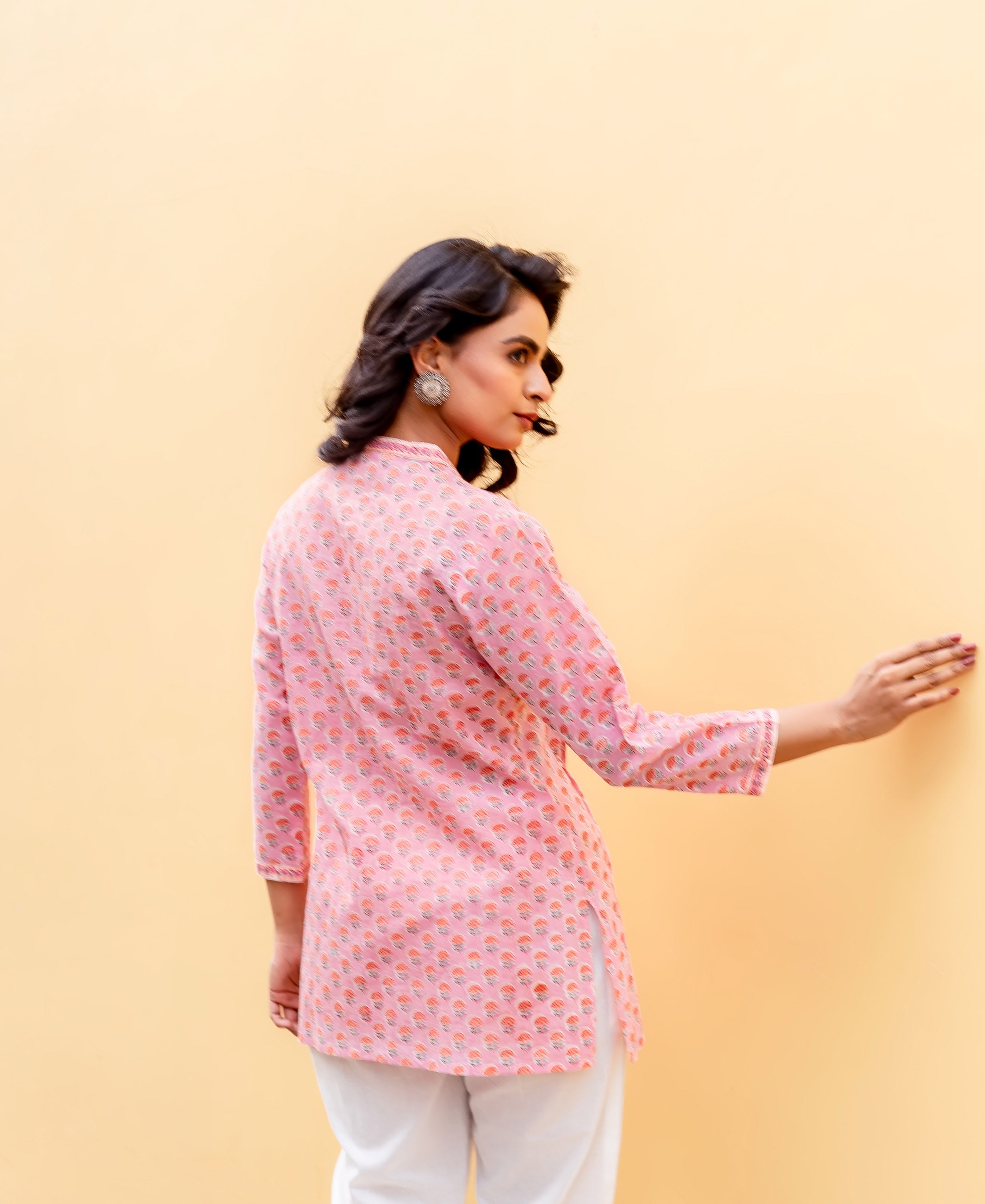 Model from back wearing a blush pink hand-block printed tunic, turning head over shoulder.