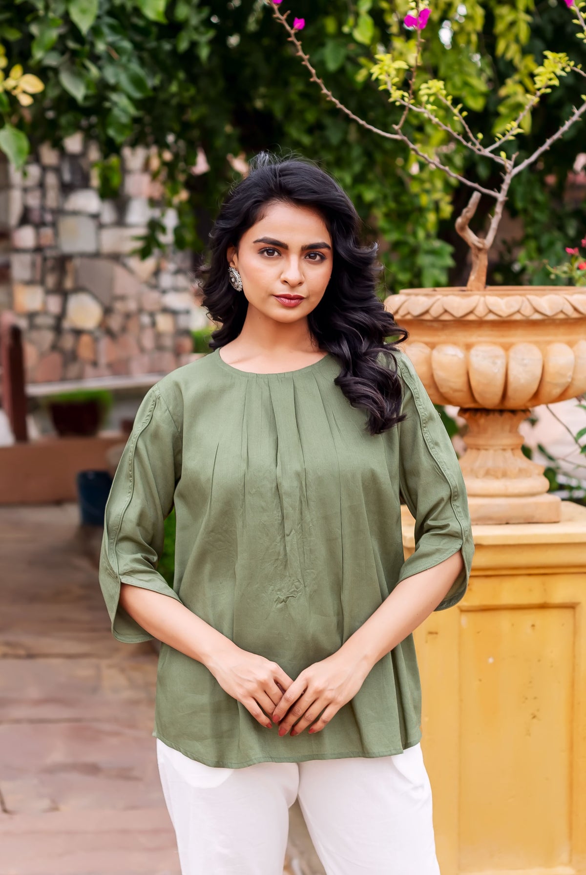 Woman in olive green tunic with front pintucks and three-quarter sleeves, standing outdoors.