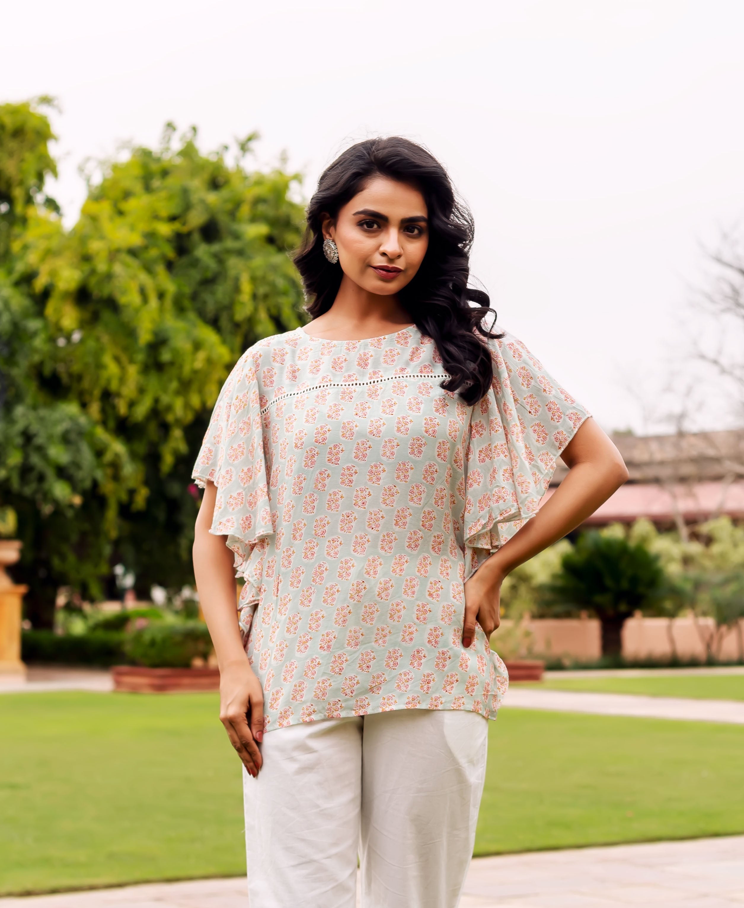 On a model, 3/4 length shot, a mint green tunic with peach floral block print and ruffled sleeves.