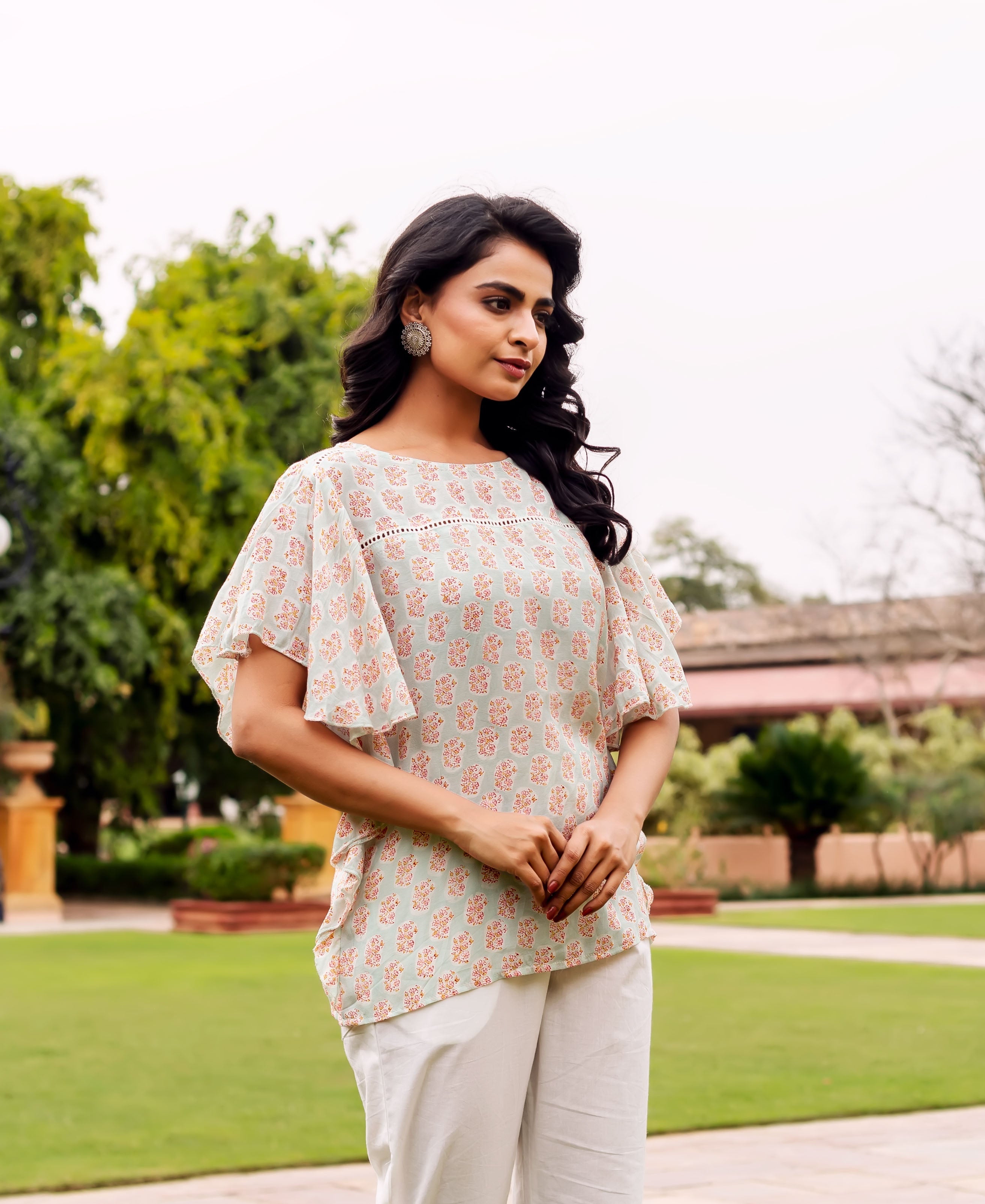 Front view: Model wears a mint tunic with red floral block print, flutter sleeves, white pants.