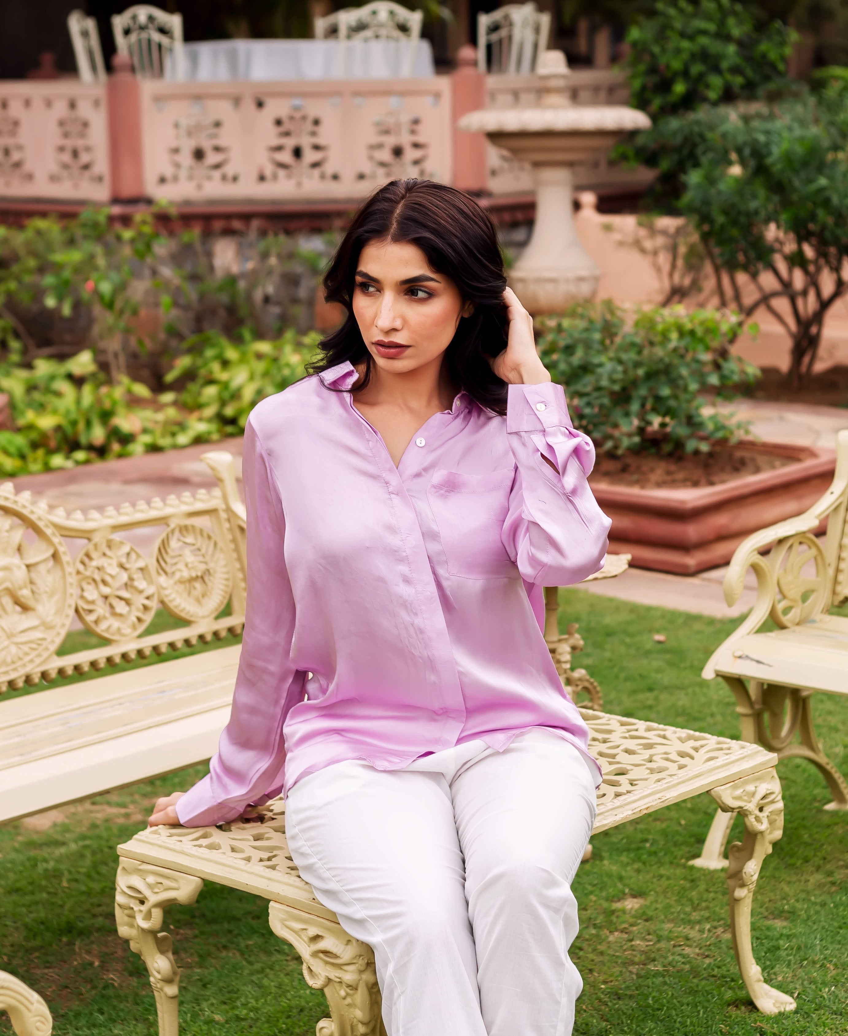 Woman wearing a pastel pink button-down shirt and white pants sitting on a bench.