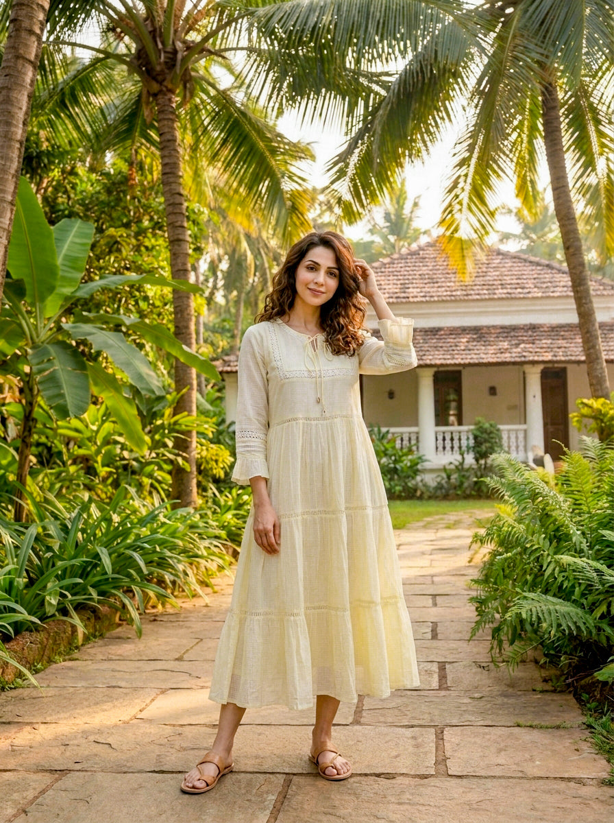 A woman in a long, ivory, tiered cotton dress with lace inserts and brown sandals.