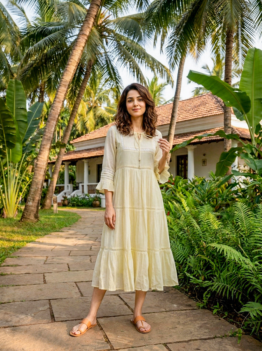 Model wearing ivory tiered dress with lace inserts and ruffled long sleeves.