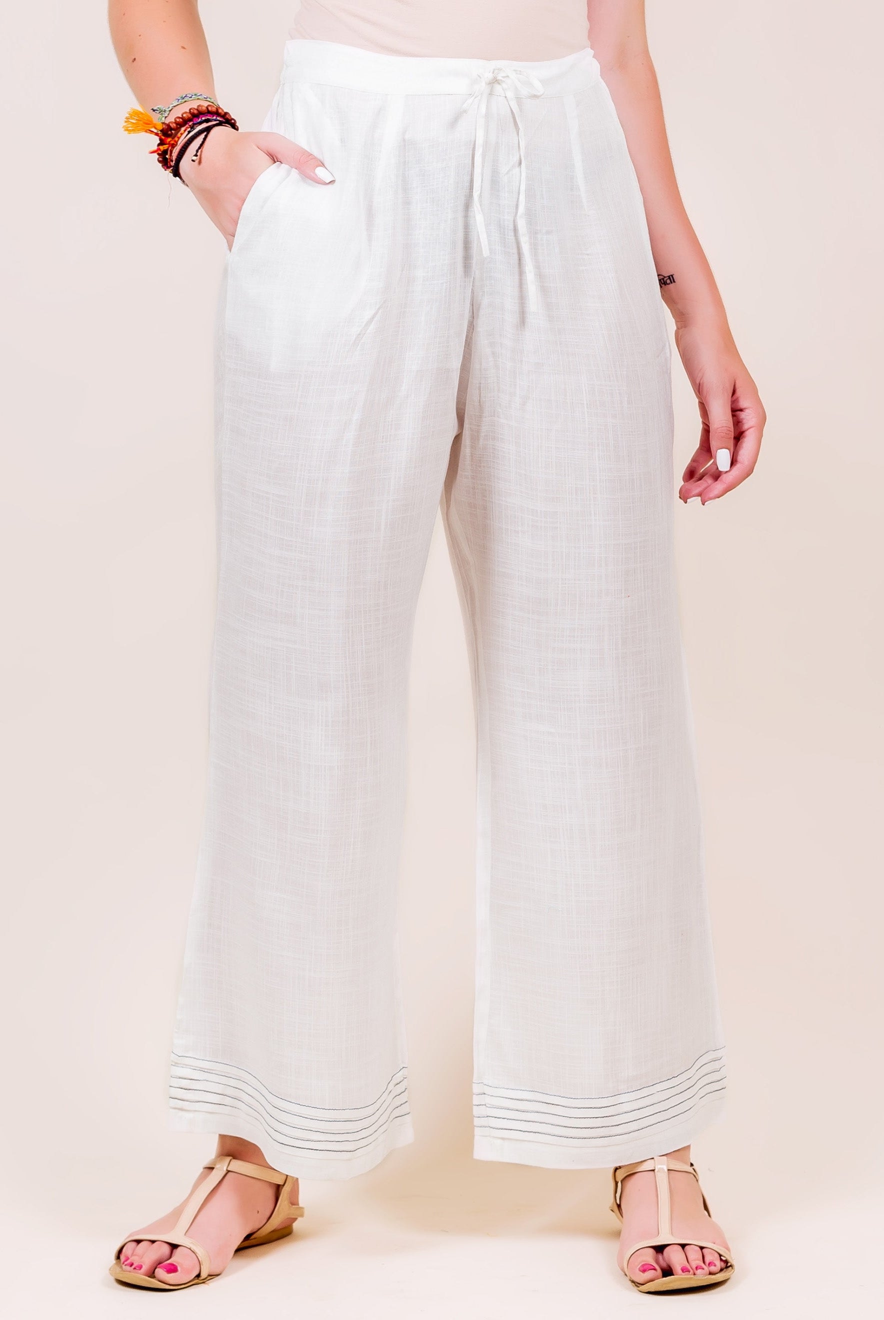 White wide-leg palazzo pants on model, drawstring waist, with subtle dark horizontal lines at hem.