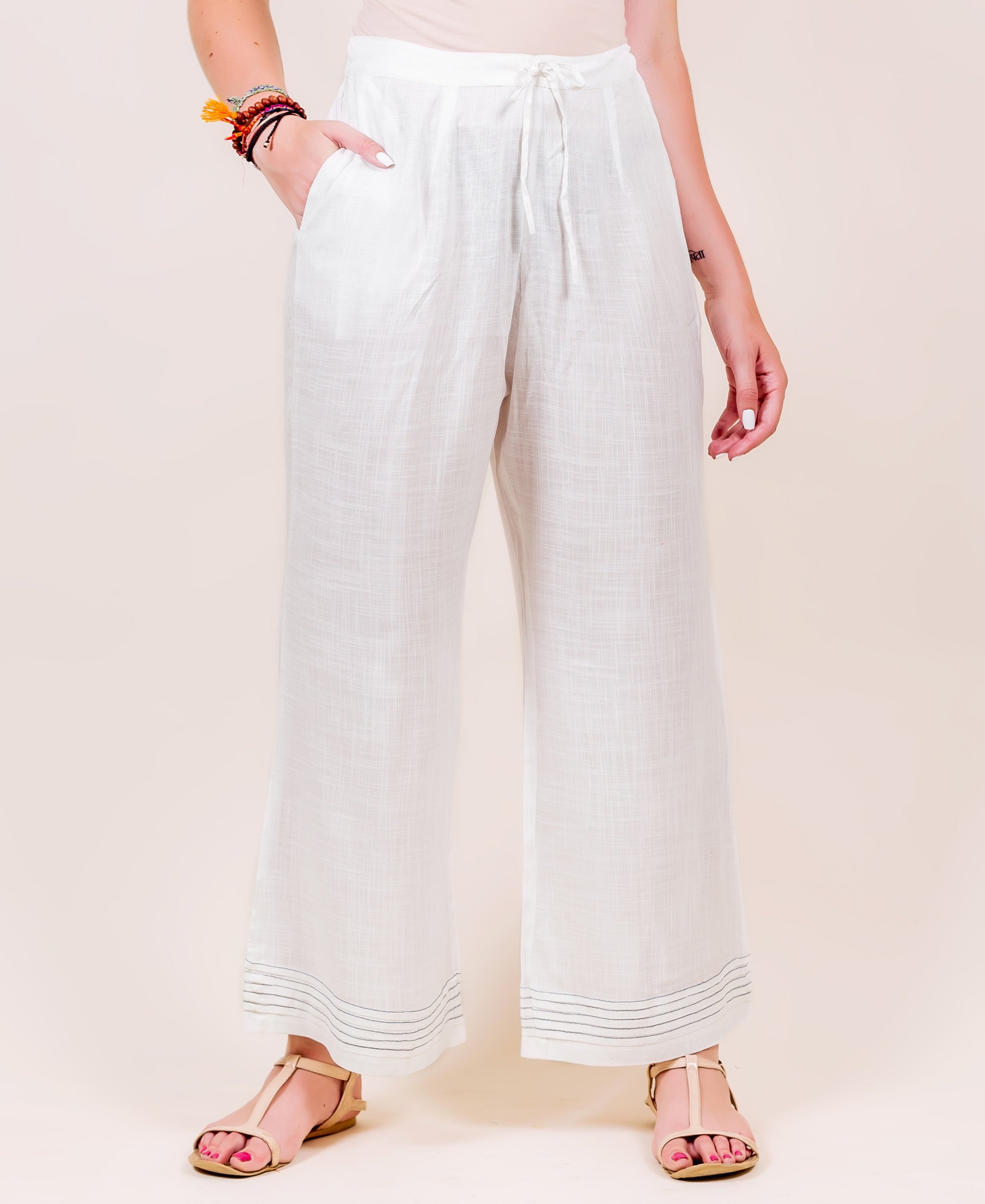 White wide-leg palazzo pants on model, drawstring waist, with subtle dark horizontal lines at hem.