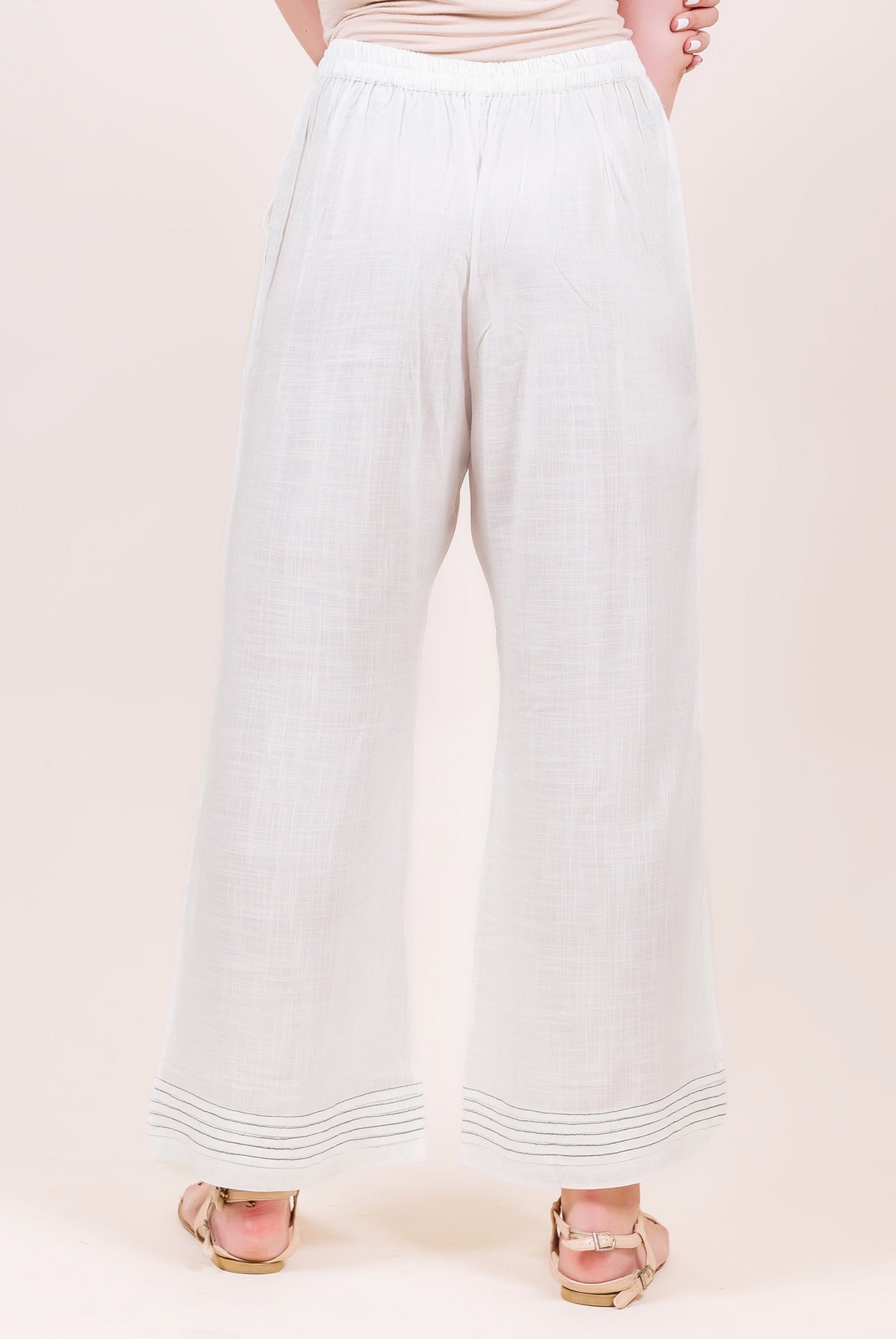 Back view of model in white flared palazzo pants featuring horizontal stitched hem lines.
