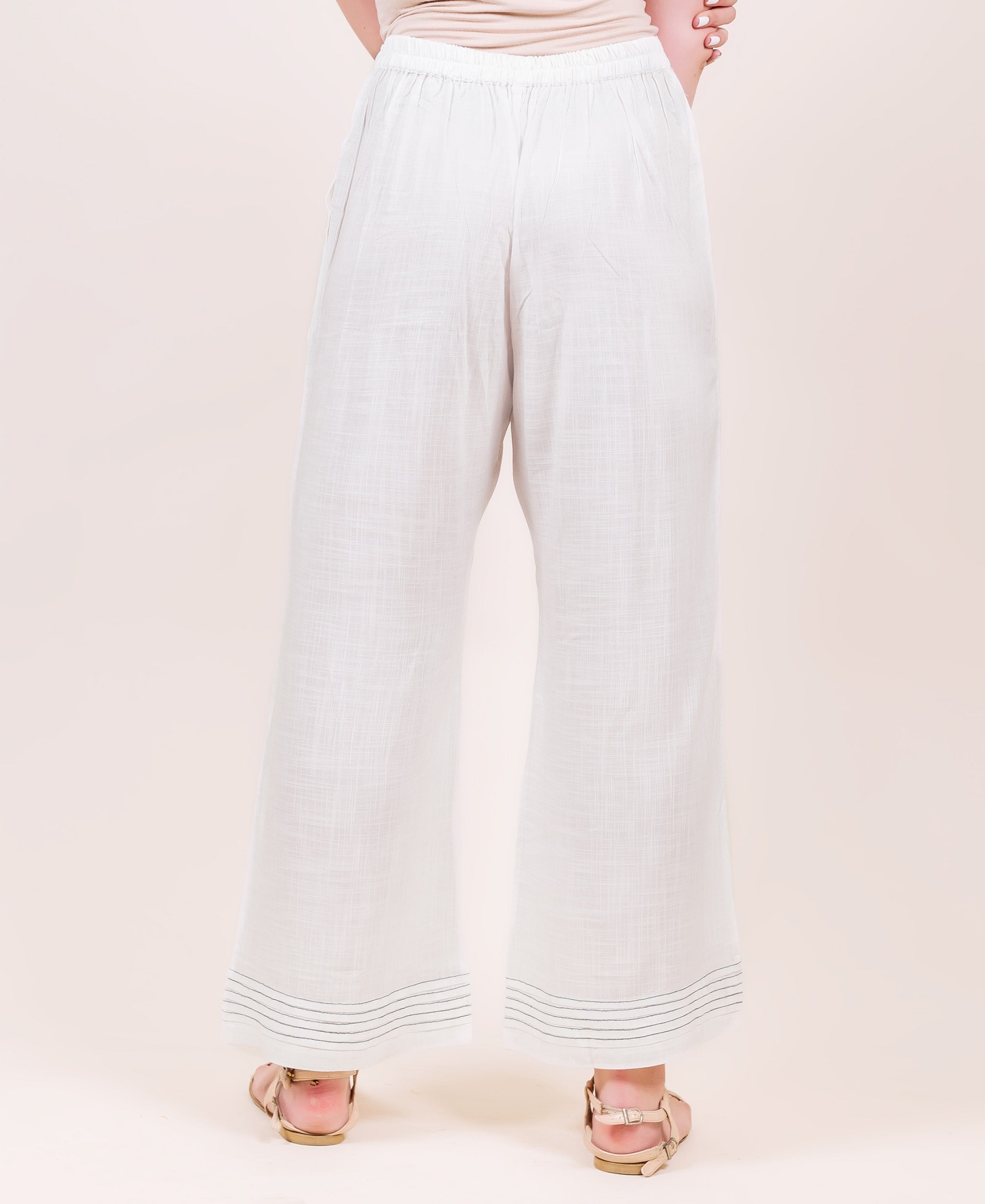 Back view of model in white flared palazzo pants featuring horizontal stitched hem lines.