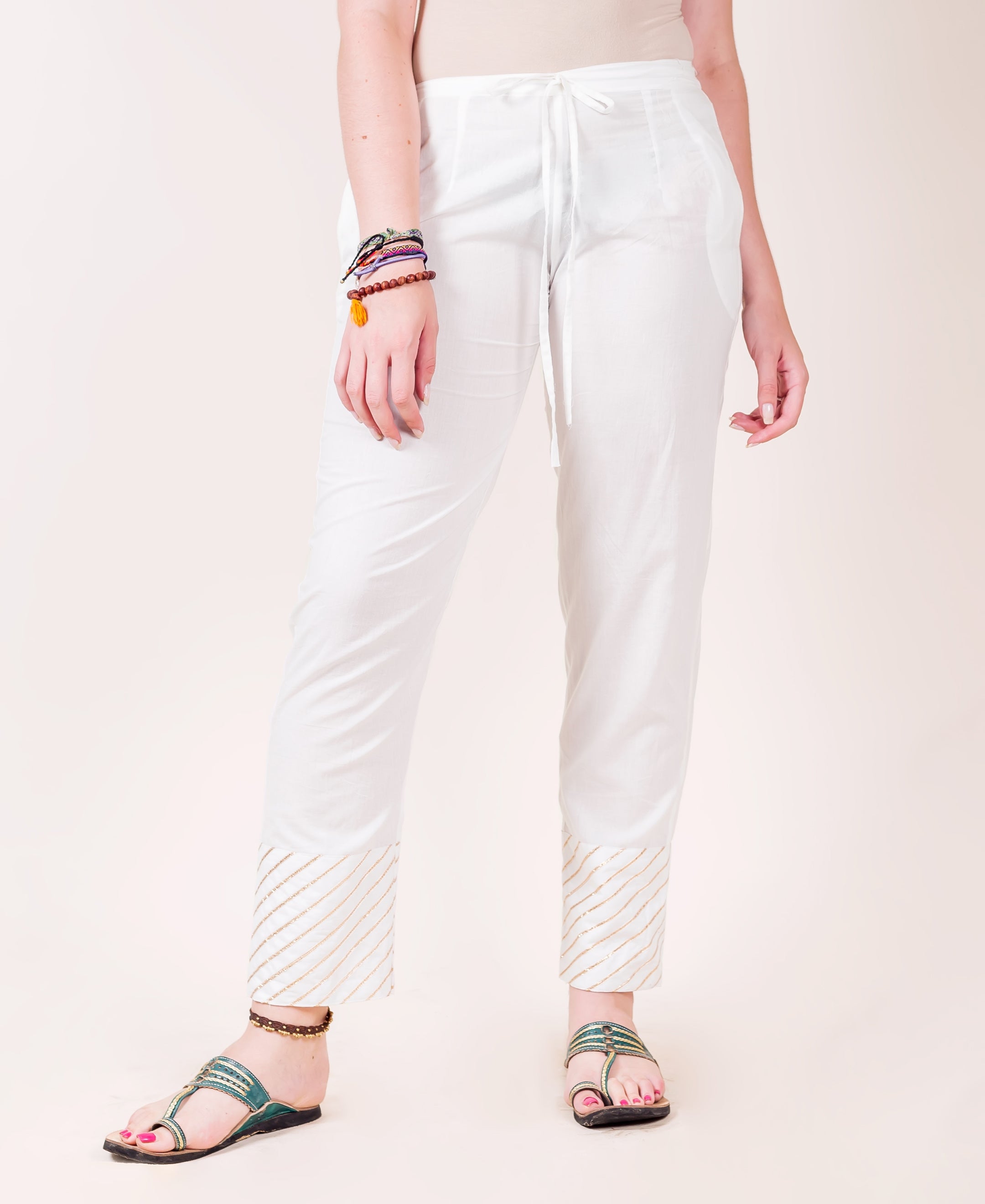 Model wears white straight pants with gold striped gota trim at the pant hem.