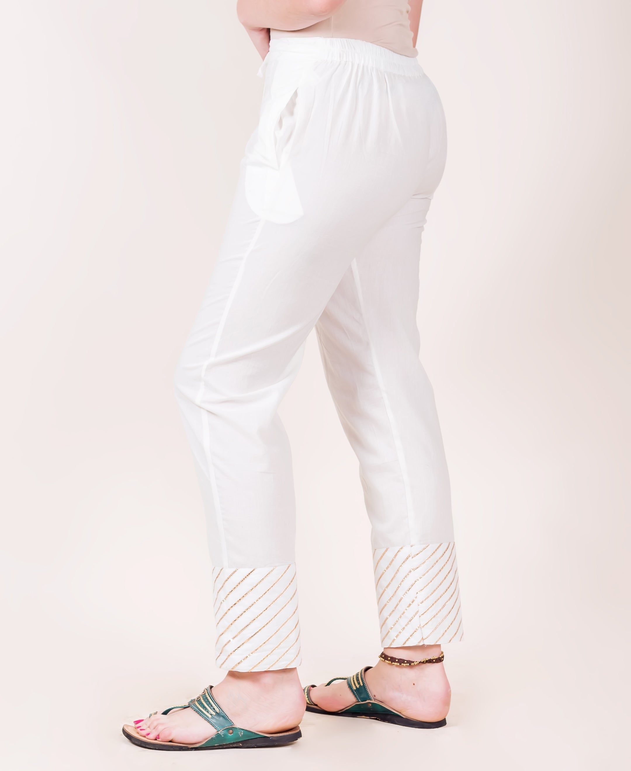White straight pants on a model, featuring gold diagonal gota trim on the cuffs.