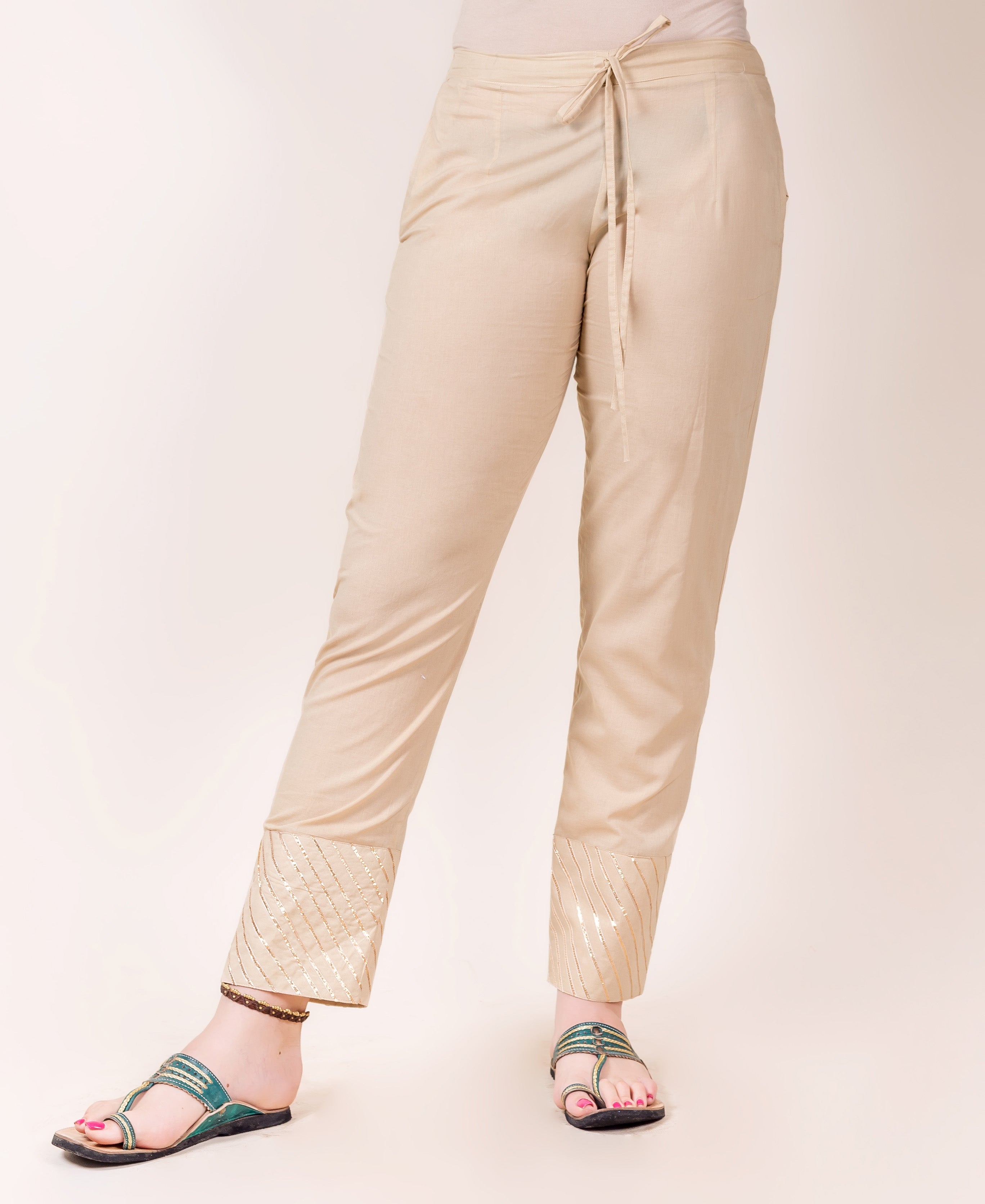 Model wears beige straight pants with golden gota trim detailing at the cuffs.