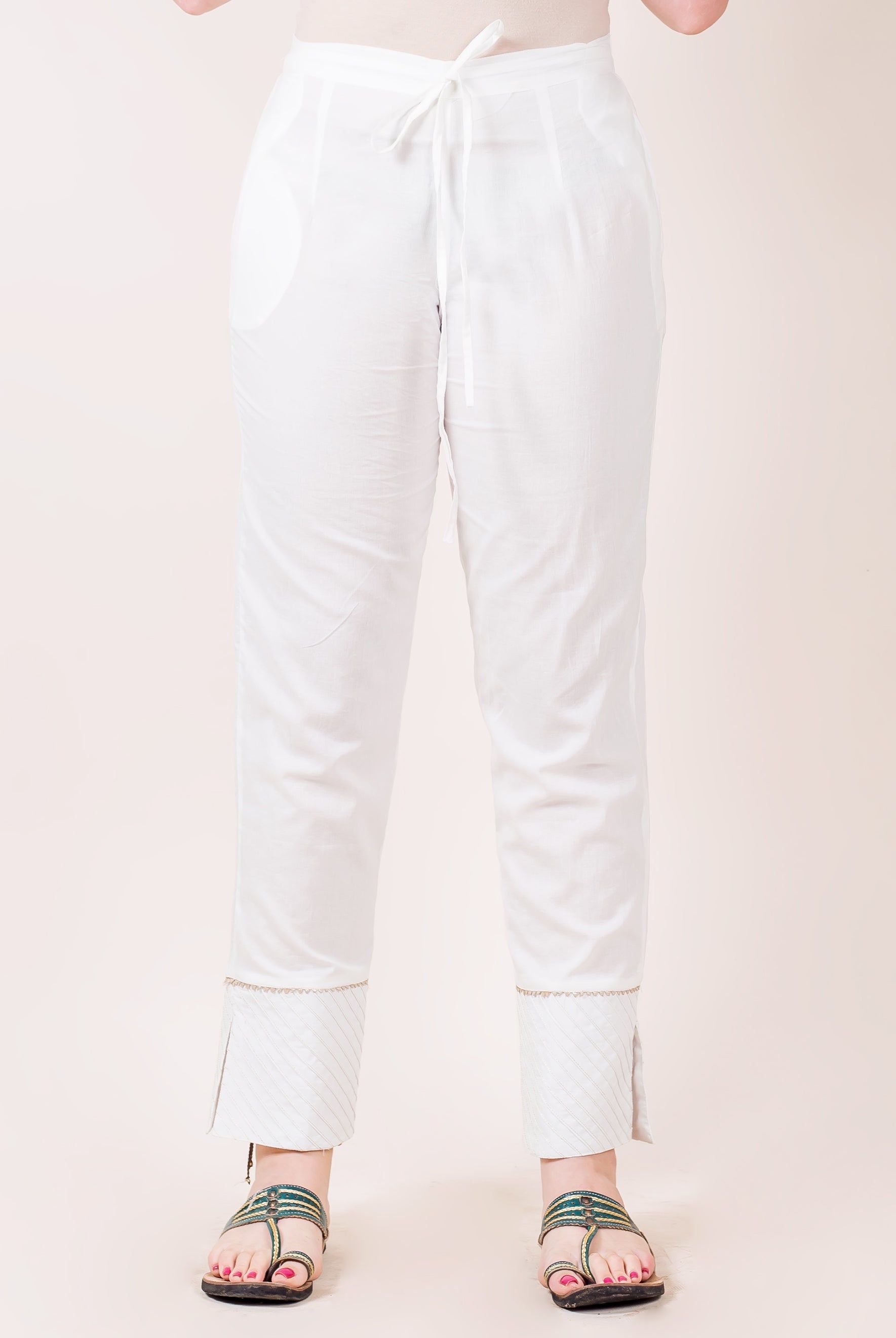 White straight pants on model, with drawstring waist and patterned hem with trim.