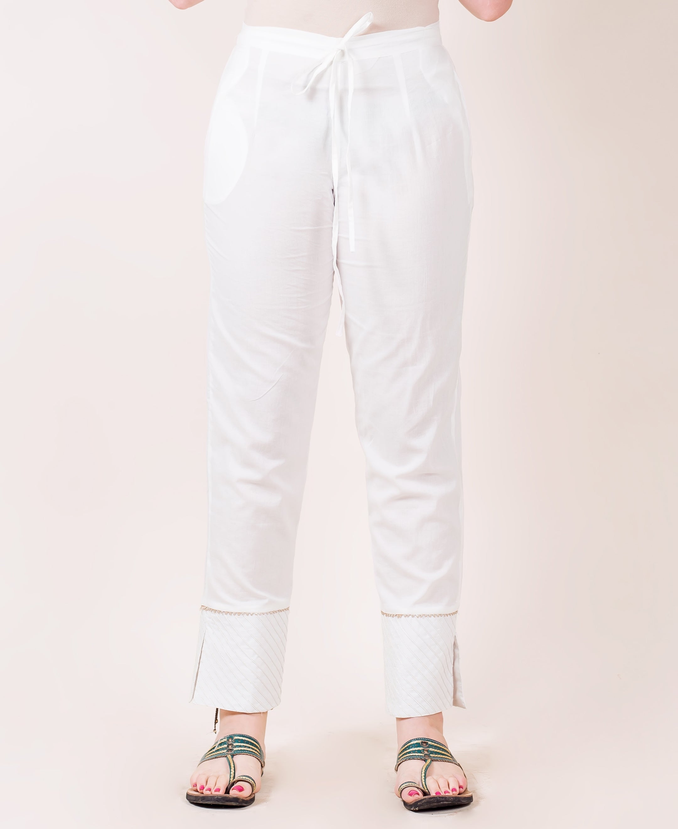 White straight pants on model, with drawstring waist and patterned hem with trim.