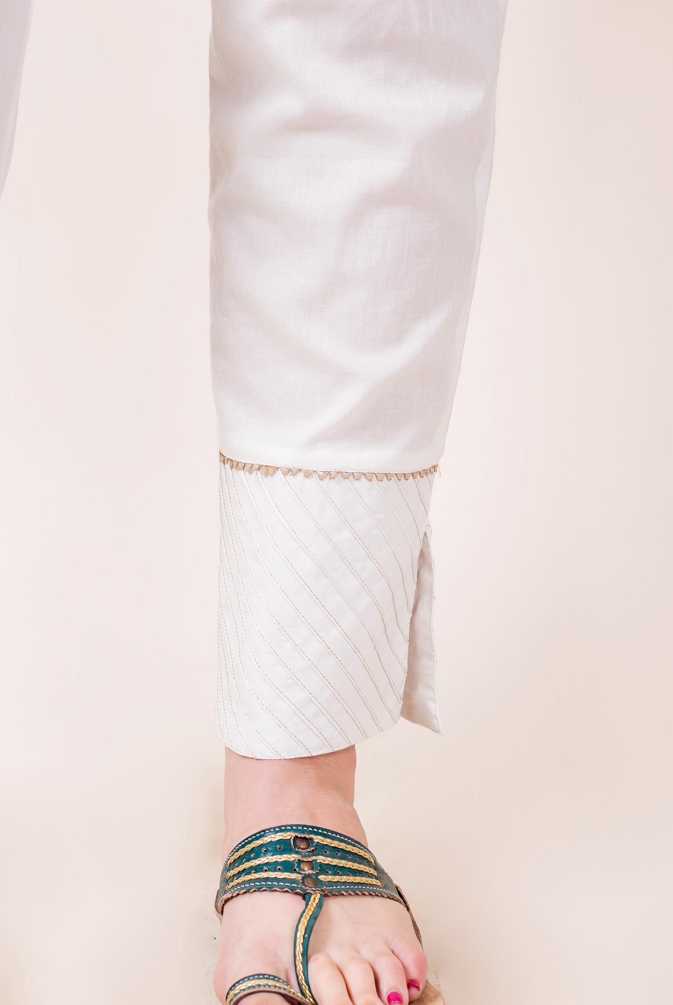 White straight pants on a model, featuring golden trim and striped cuffs with slits.