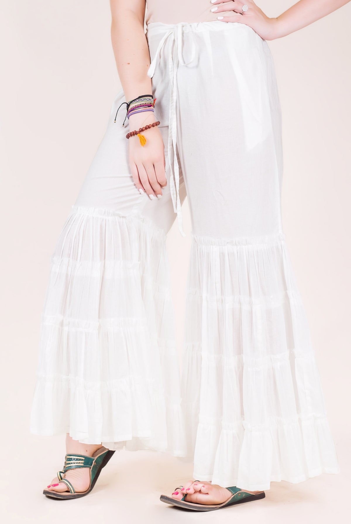 White tiered sharara pants on a model, featuring wide ruffled layers and a drawstring waist.