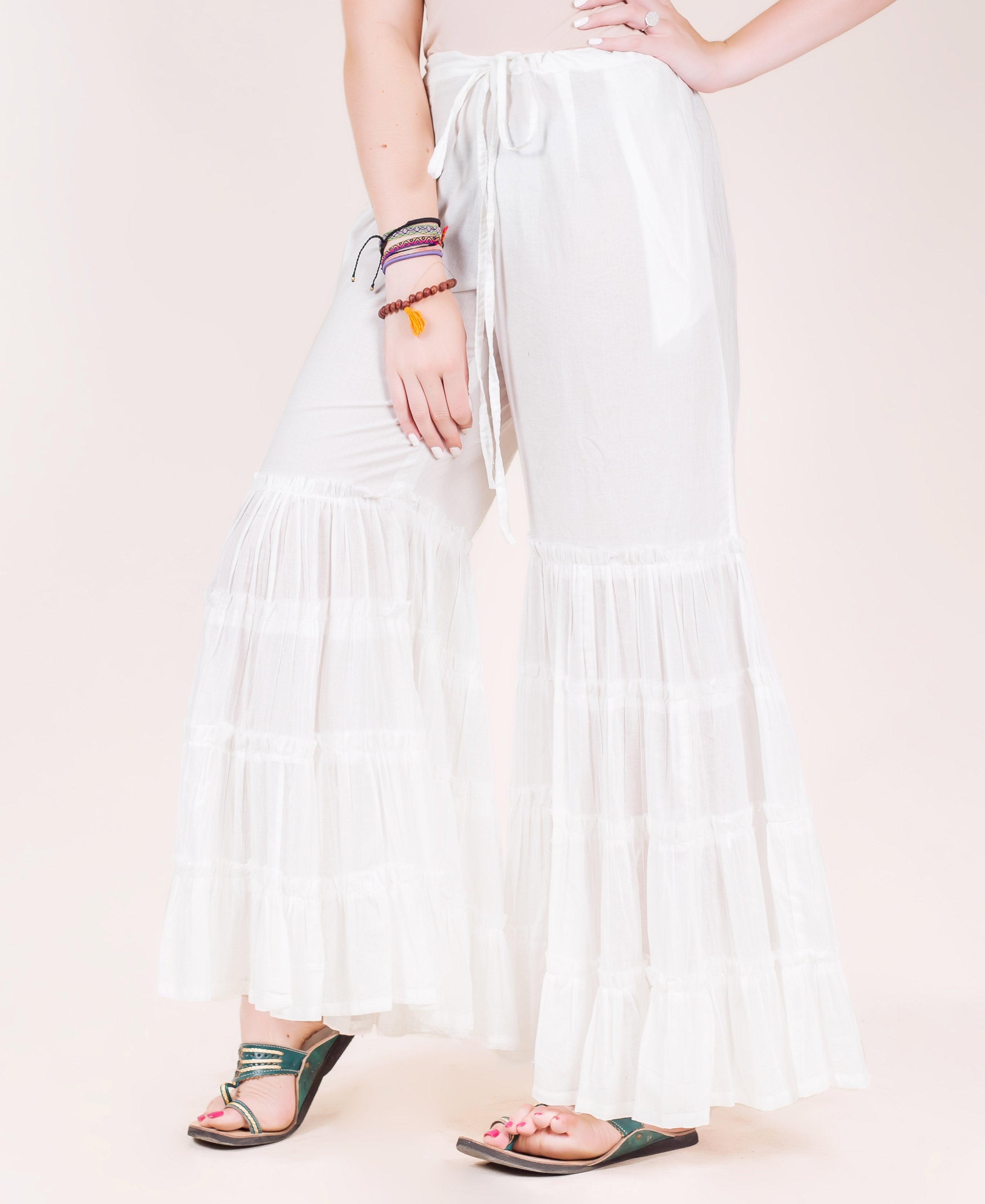 White tiered sharara pants on a model, featuring wide ruffled layers and a drawstring waist.