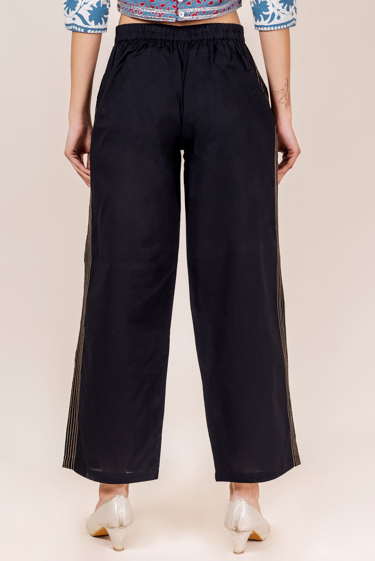 Model from back in black palazzo pants featuring vertical gold embroidered stripes.