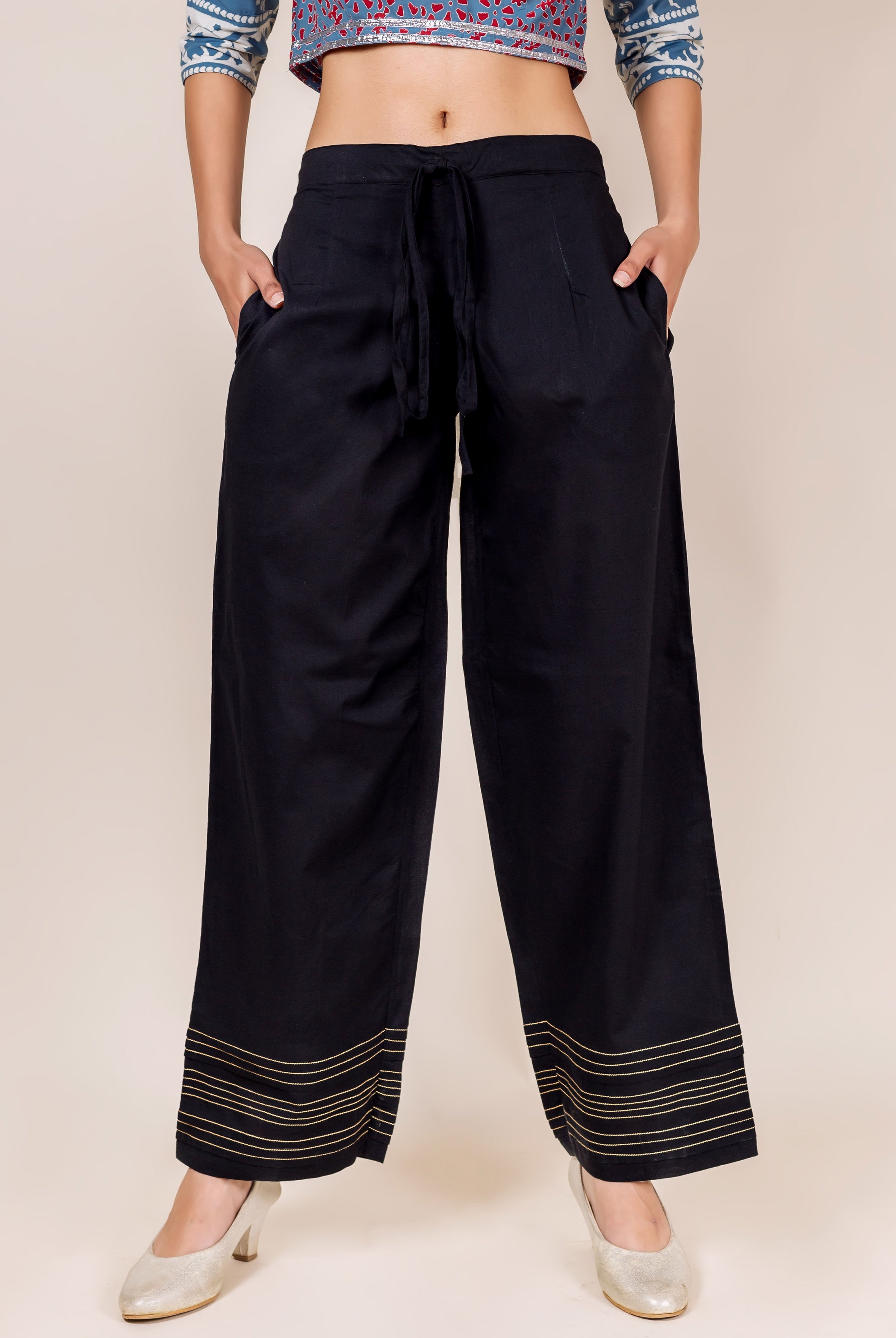 Model stands in black palazzo pants featuring golden embroidered horizontal lines at the hem.
