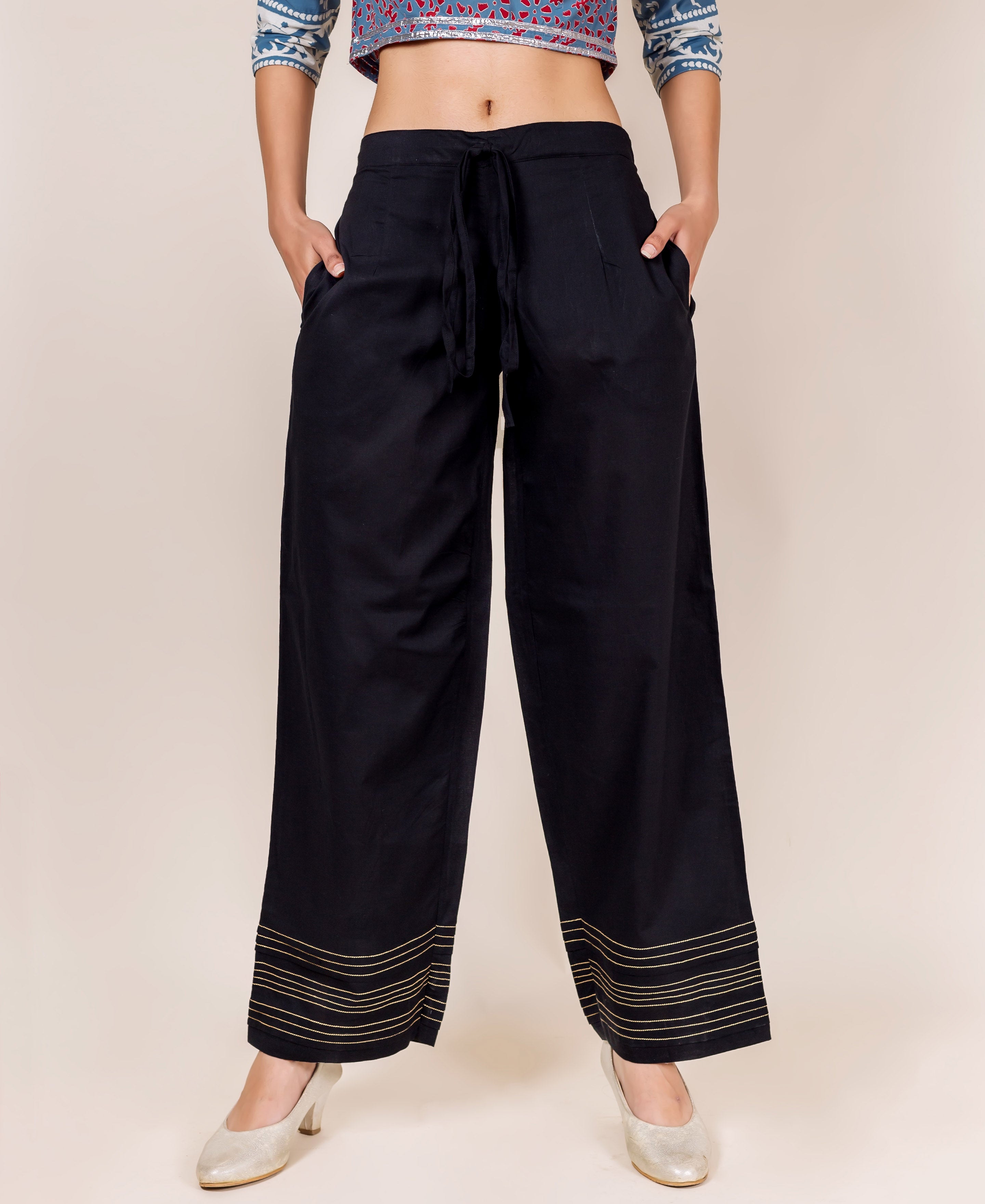Model stands in black palazzo pants featuring golden embroidered horizontal lines at the hem.