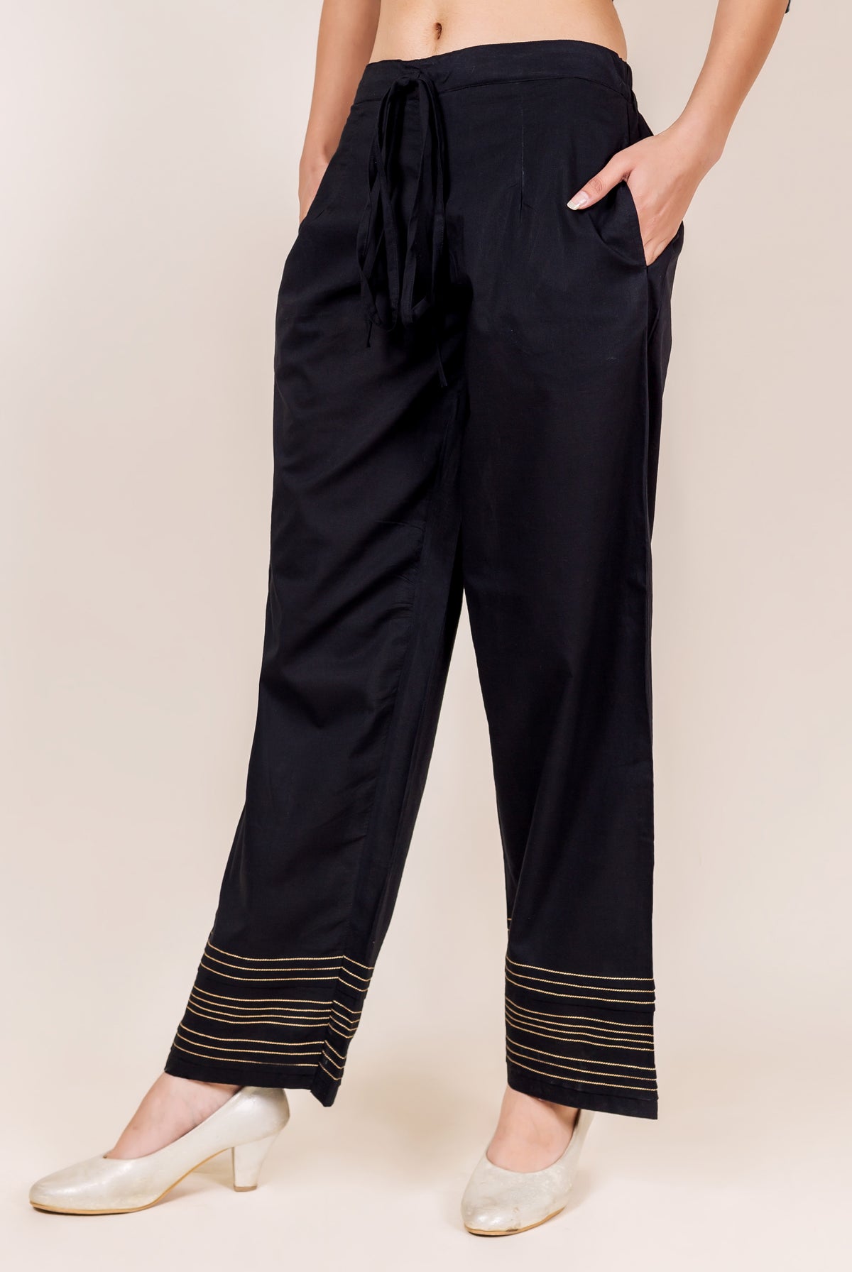 Black palazzo pants with golden embroidered horizontal lines on the cuffs, front view.