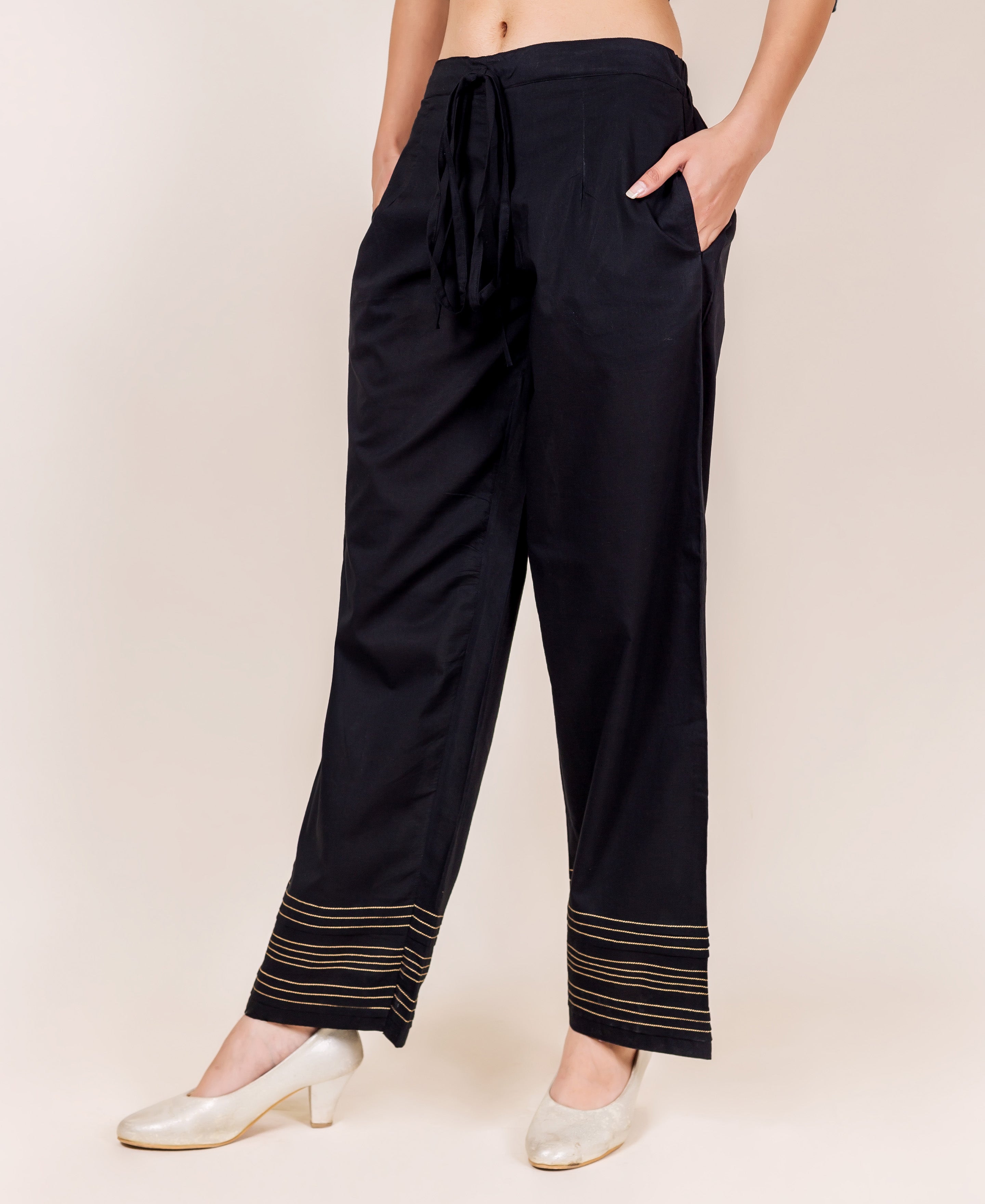 Black palazzo pants with golden embroidered horizontal lines on the cuffs, front view.