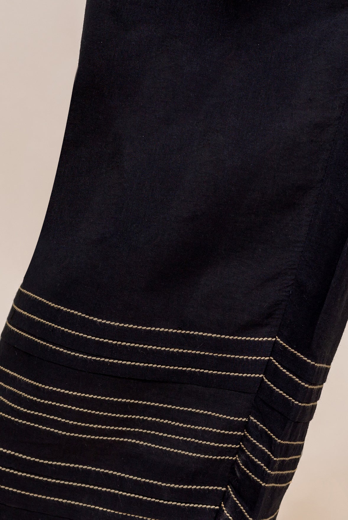 Close-up of black palazzo pants bottom showing horizontal gold embroidered lines and pleats.