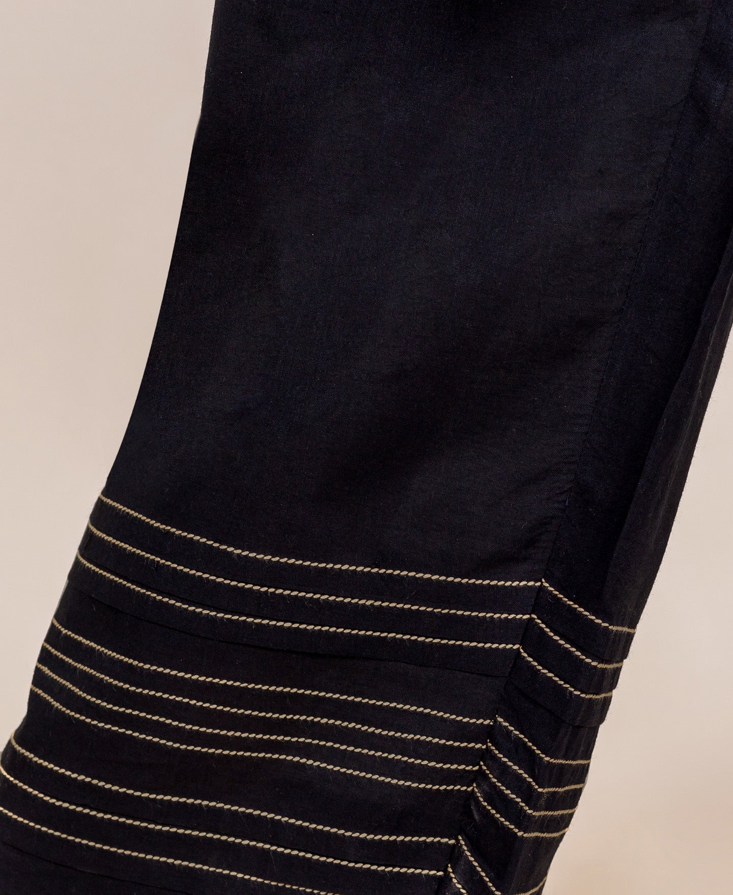 Close-up of black palazzo pants bottom showing horizontal gold embroidered lines and pleats.