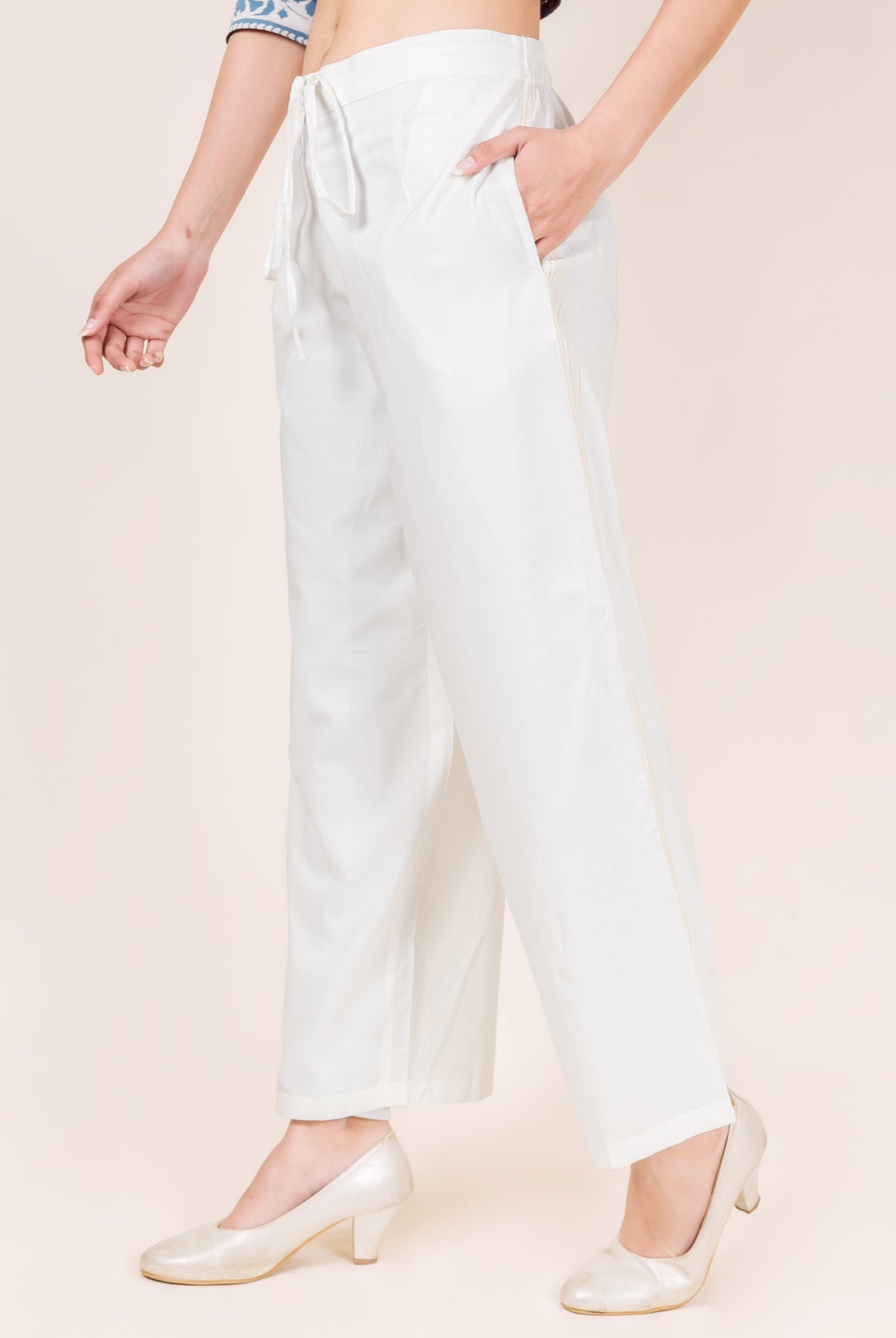 White embroidered palazzo pants on a model, side view, with drawstring waist.
