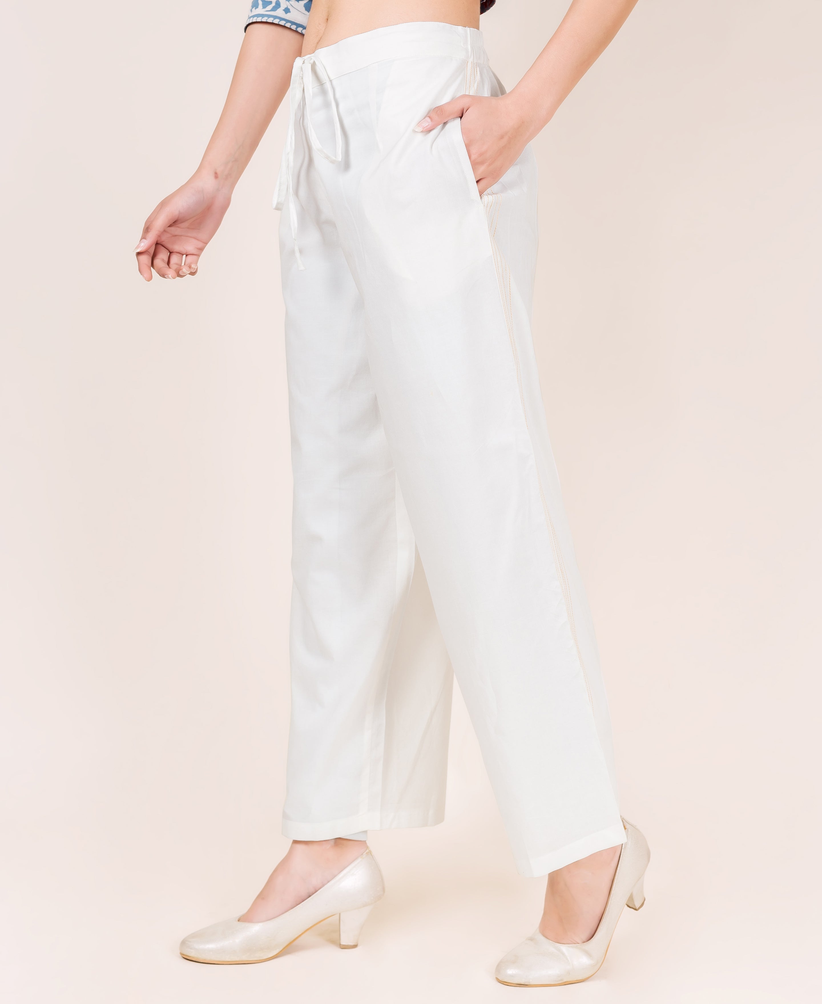 White embroidered palazzo pants on a model, side view, with drawstring waist.