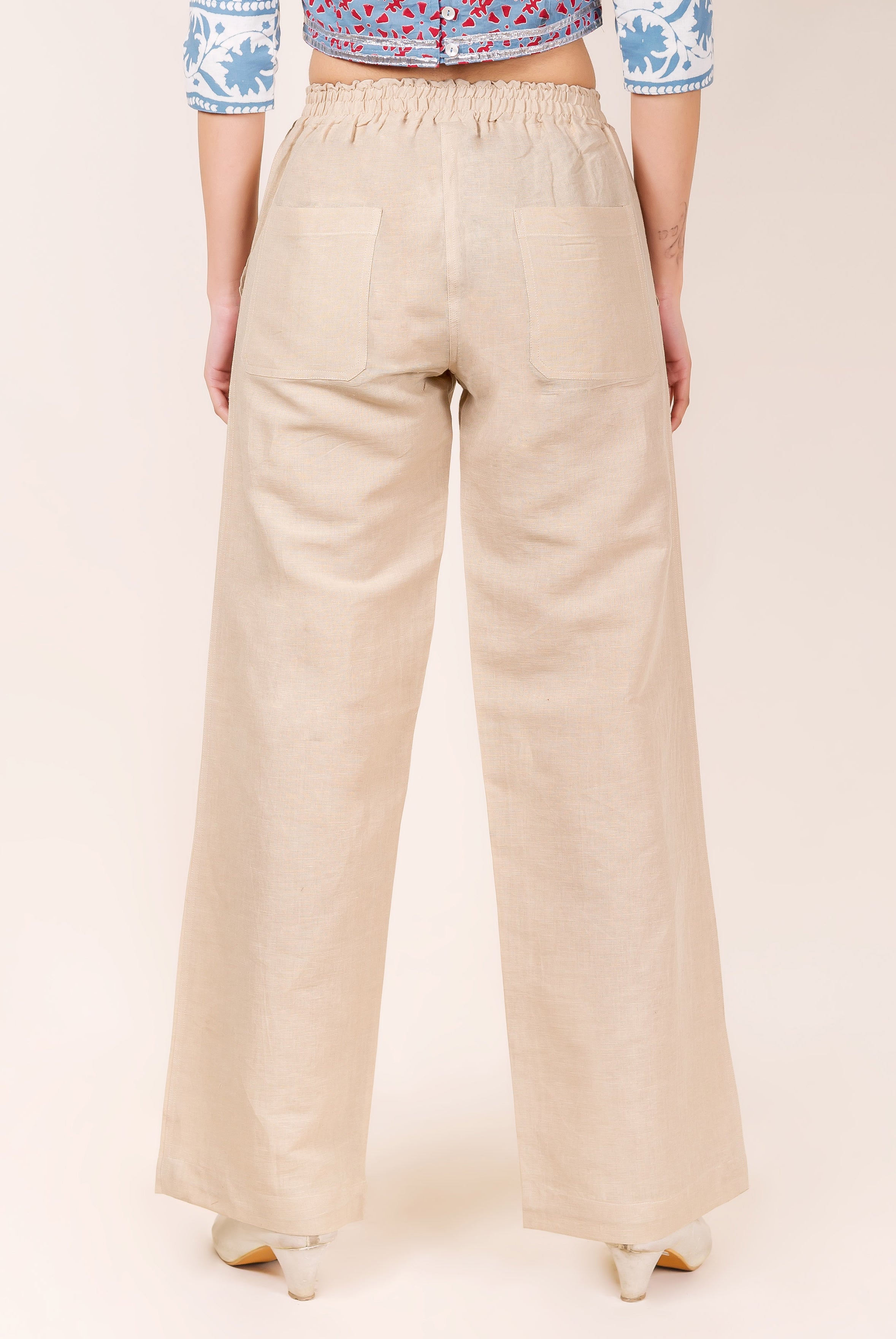 Model back, solid beige linen wide-leg pants with elastic waist and patch pockets.