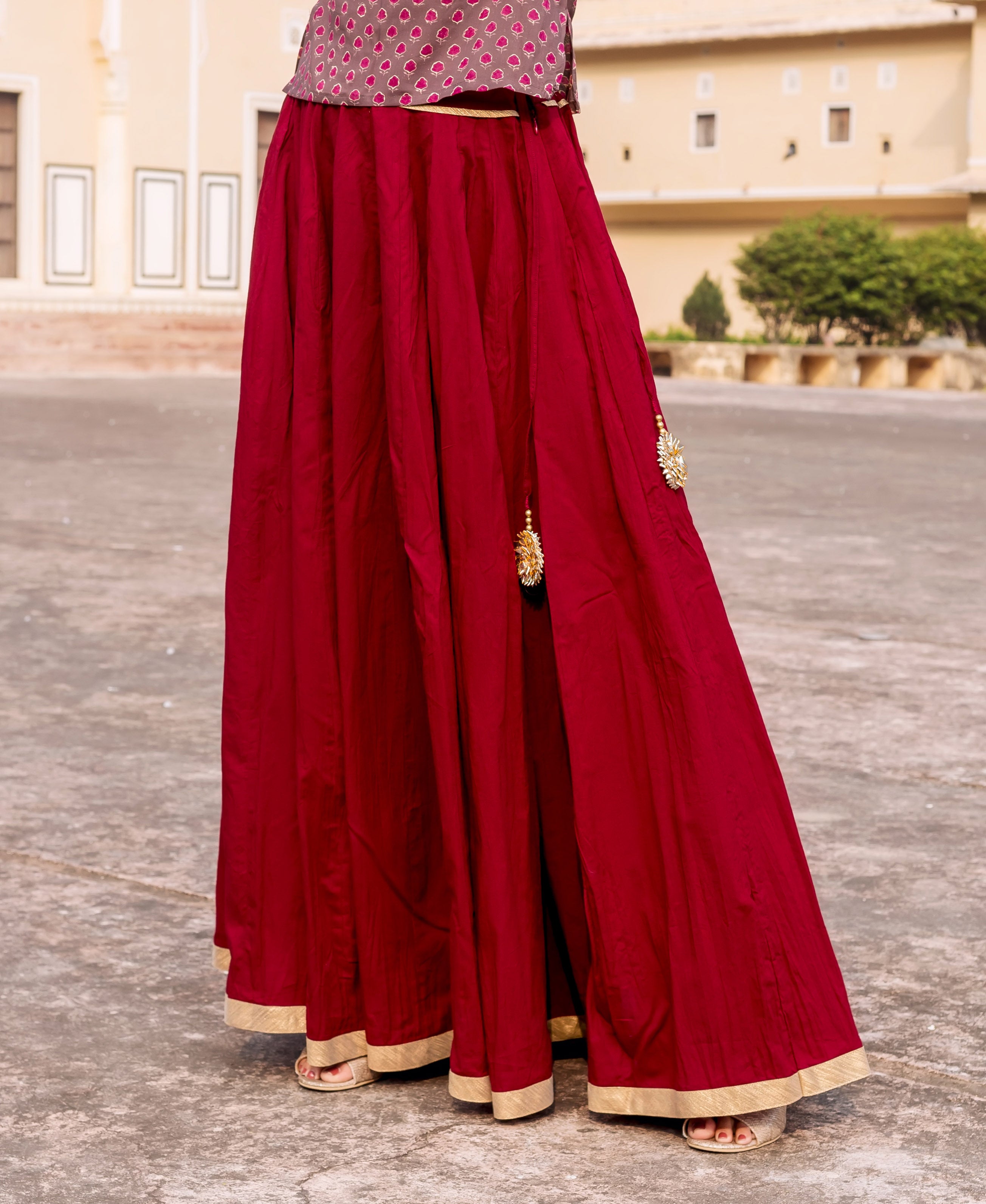 Full length maroon skirt with golden gotta trims, side slit, and tassels, worn by model.