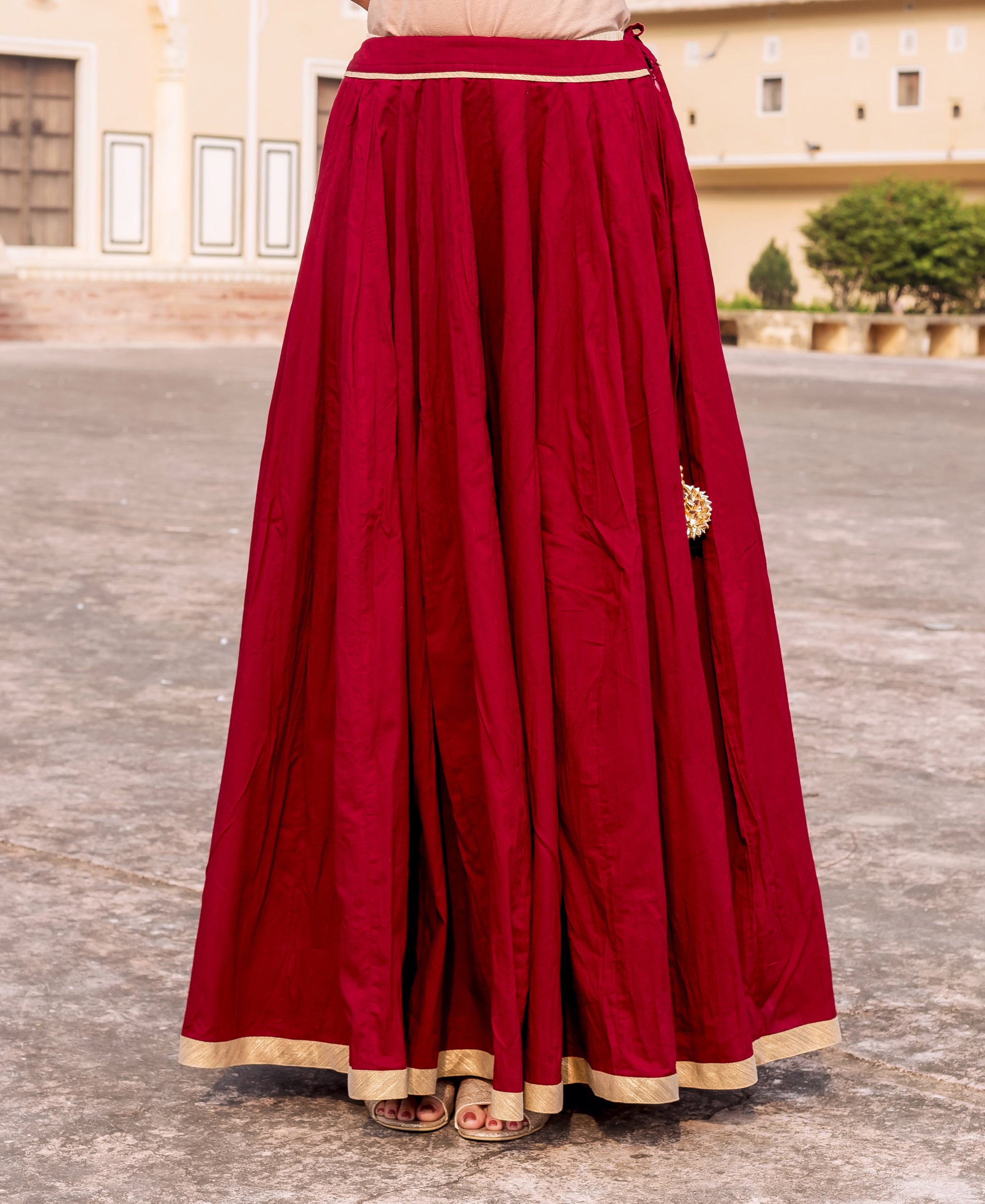 Model wearing a flowing maroon skirt with golden gotta trims at the waist and hem.