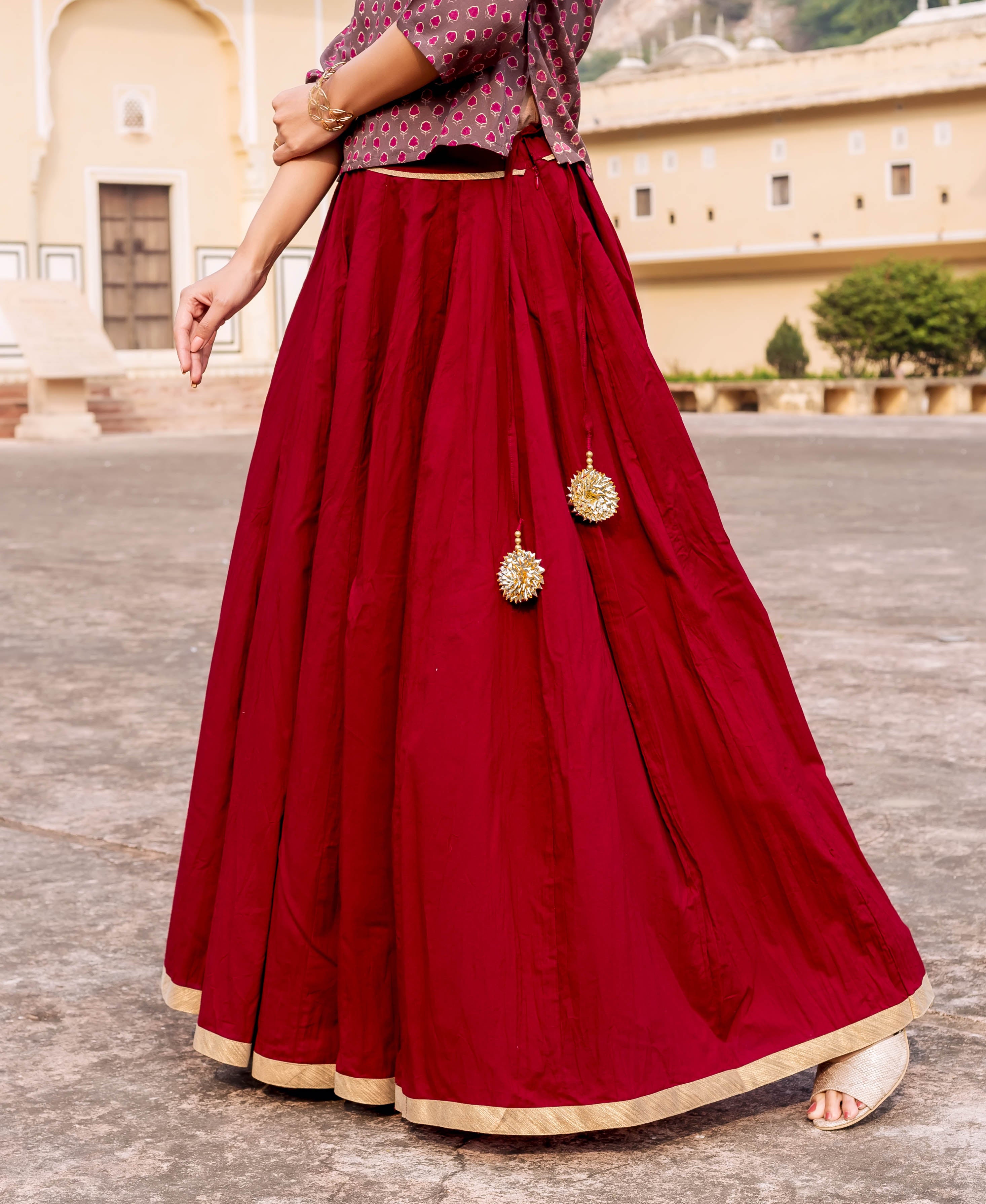 Maroon skirt with gold trim and tassels, model standing outdoors in traditional Indian clothing.
