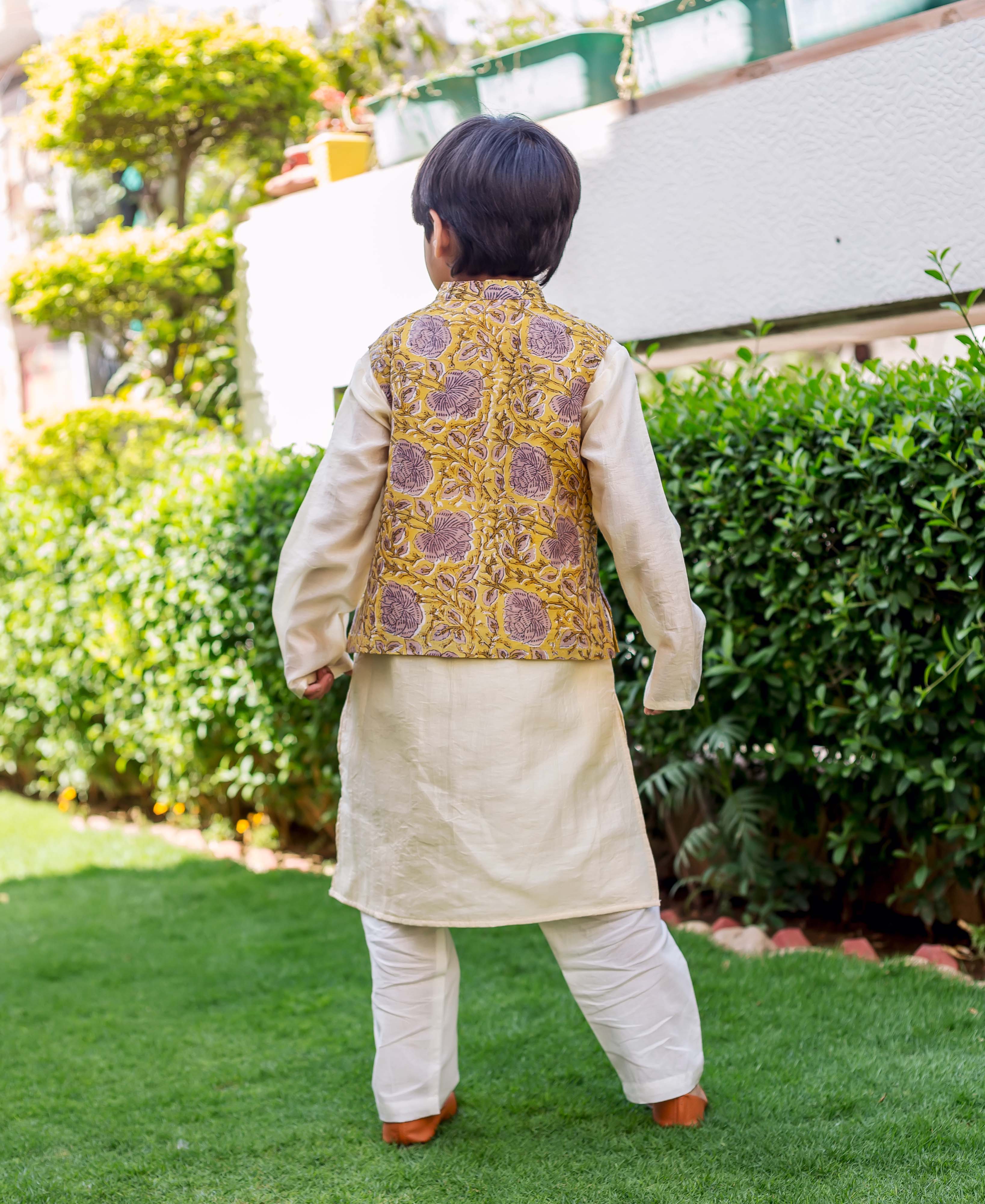 Child model, back view, cream kurta set with yellow and grey block-printed waistcoat.