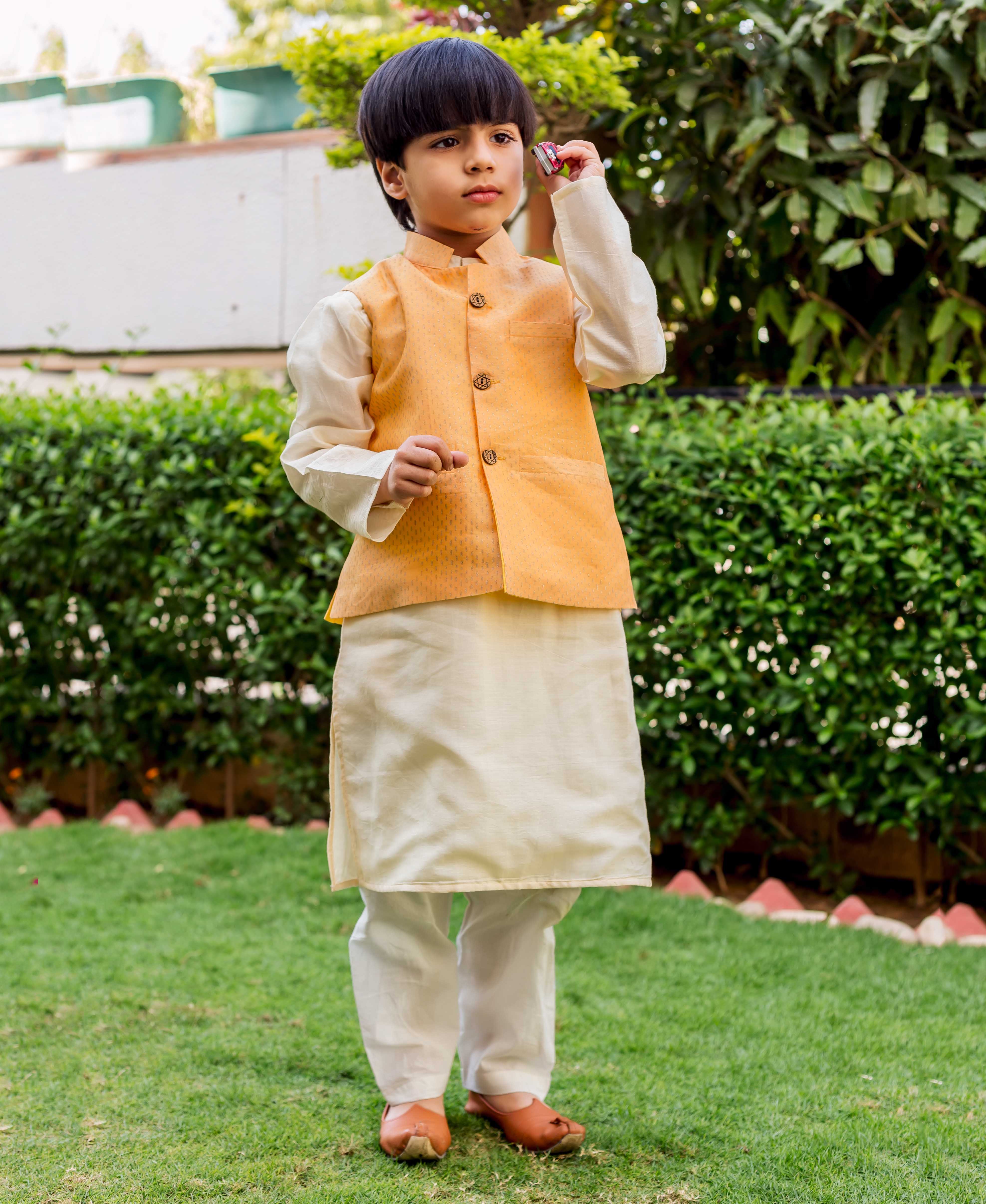 Young boy models full-length yellow Chanderi waistcoat with subtle dot print over cream kurta.