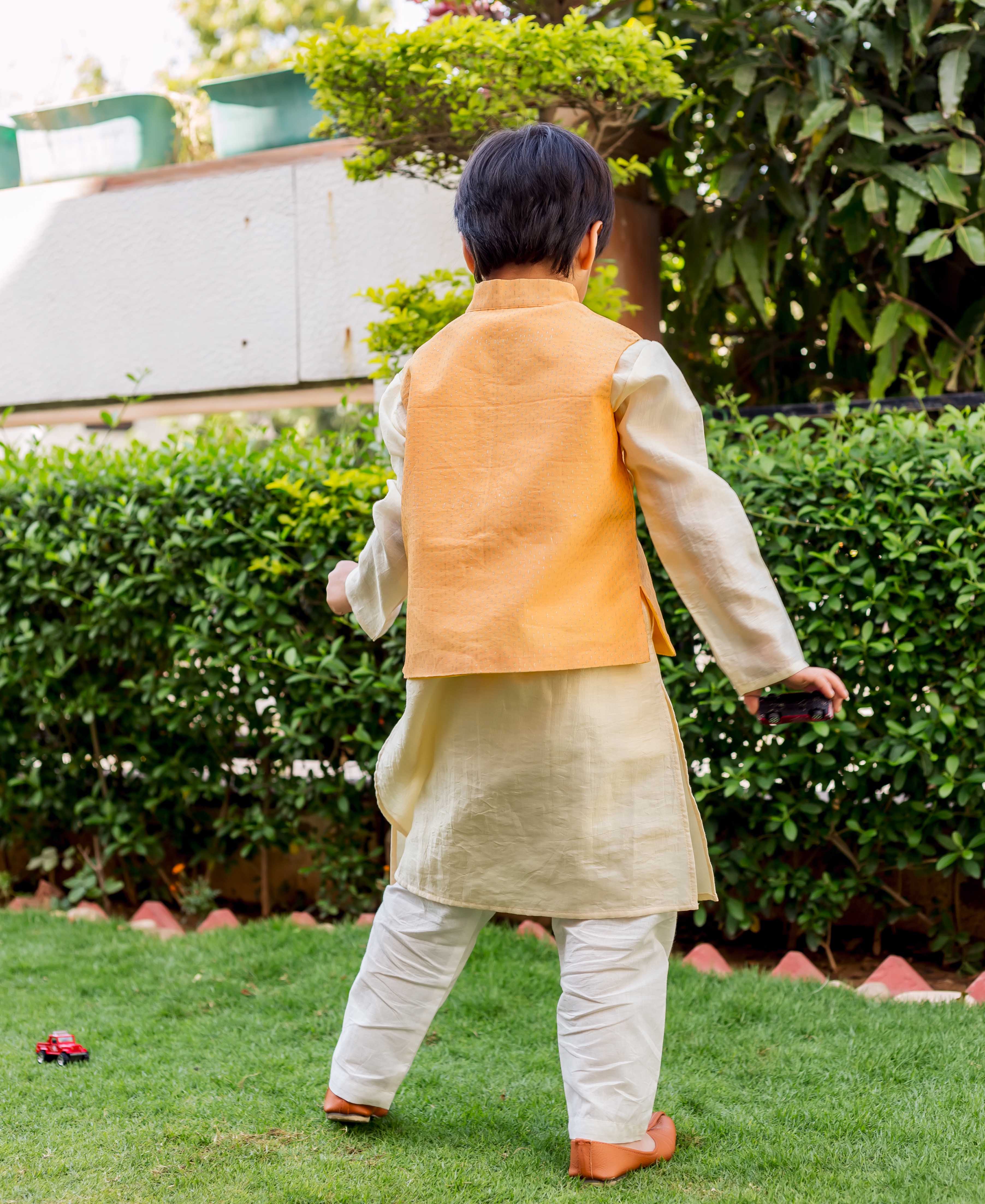Yellow hand-block-printed Chanderi waistcoat on young boy, back view, over cream kurta and white pajamas.