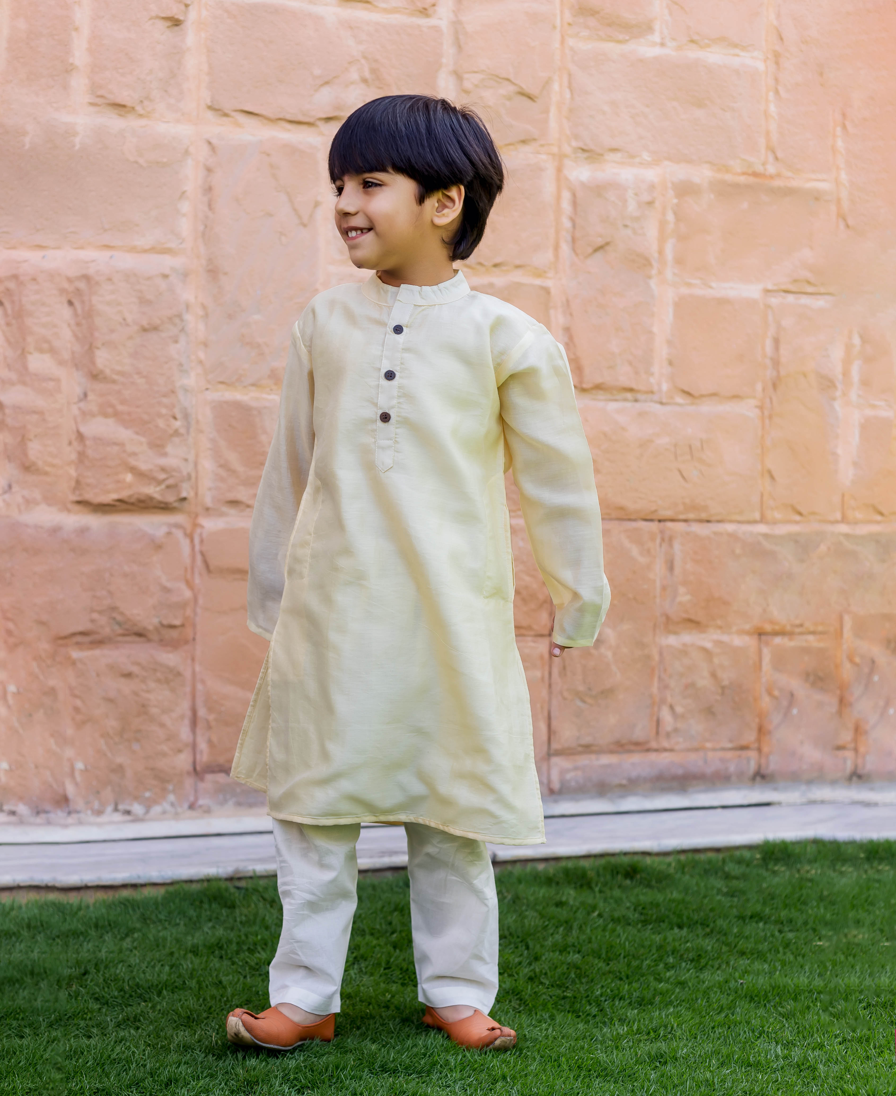 Smiling boy in a crème kurta and white pajama full look with brown mojaris.
