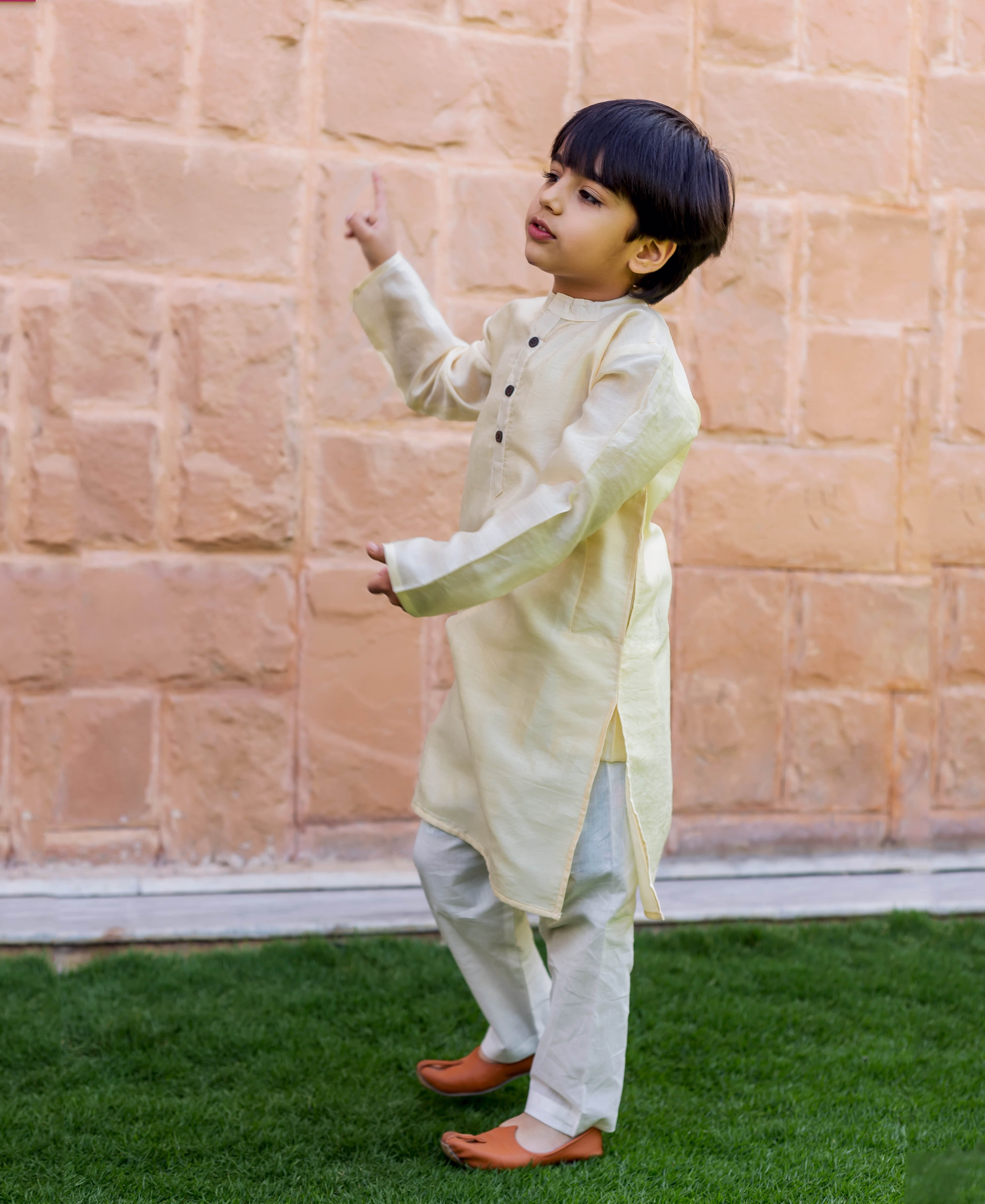 Side view of a child wearing a plain crème chanderi kurta and white pajama set.