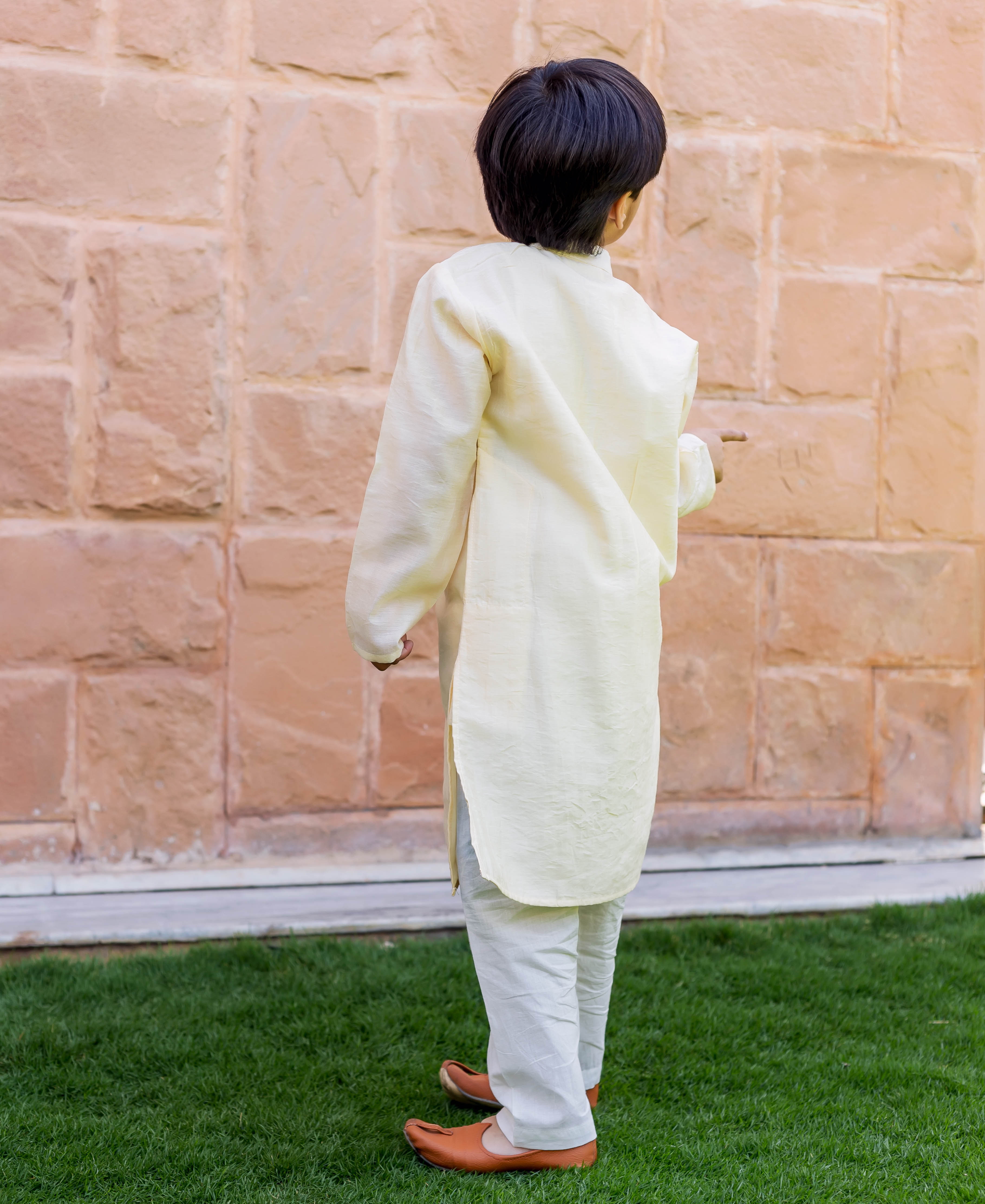 Child model in full crème kurta and white pajama set, back view.