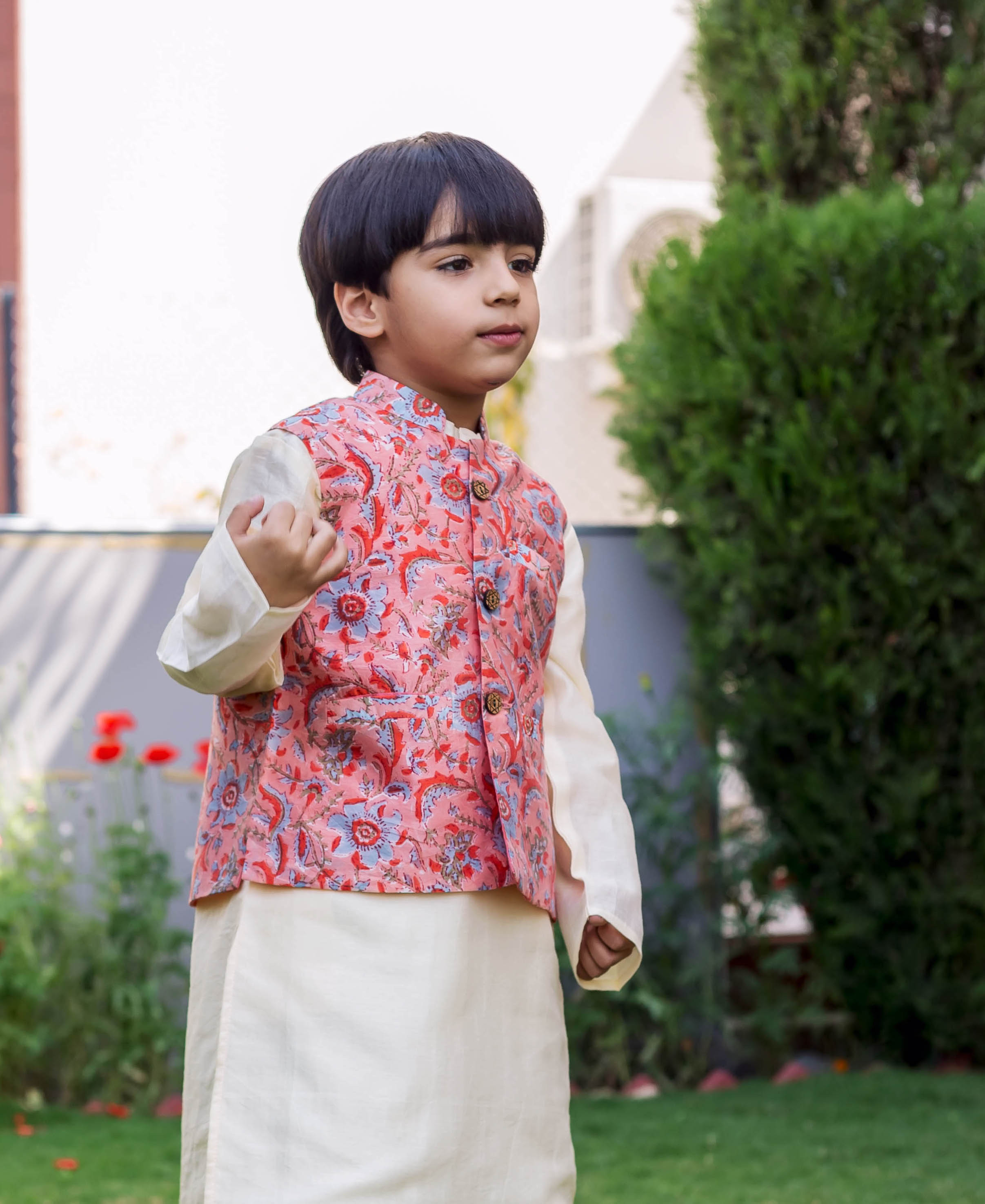 A young boy wearing a peach chanderi printed waist coat with a floral pattern.