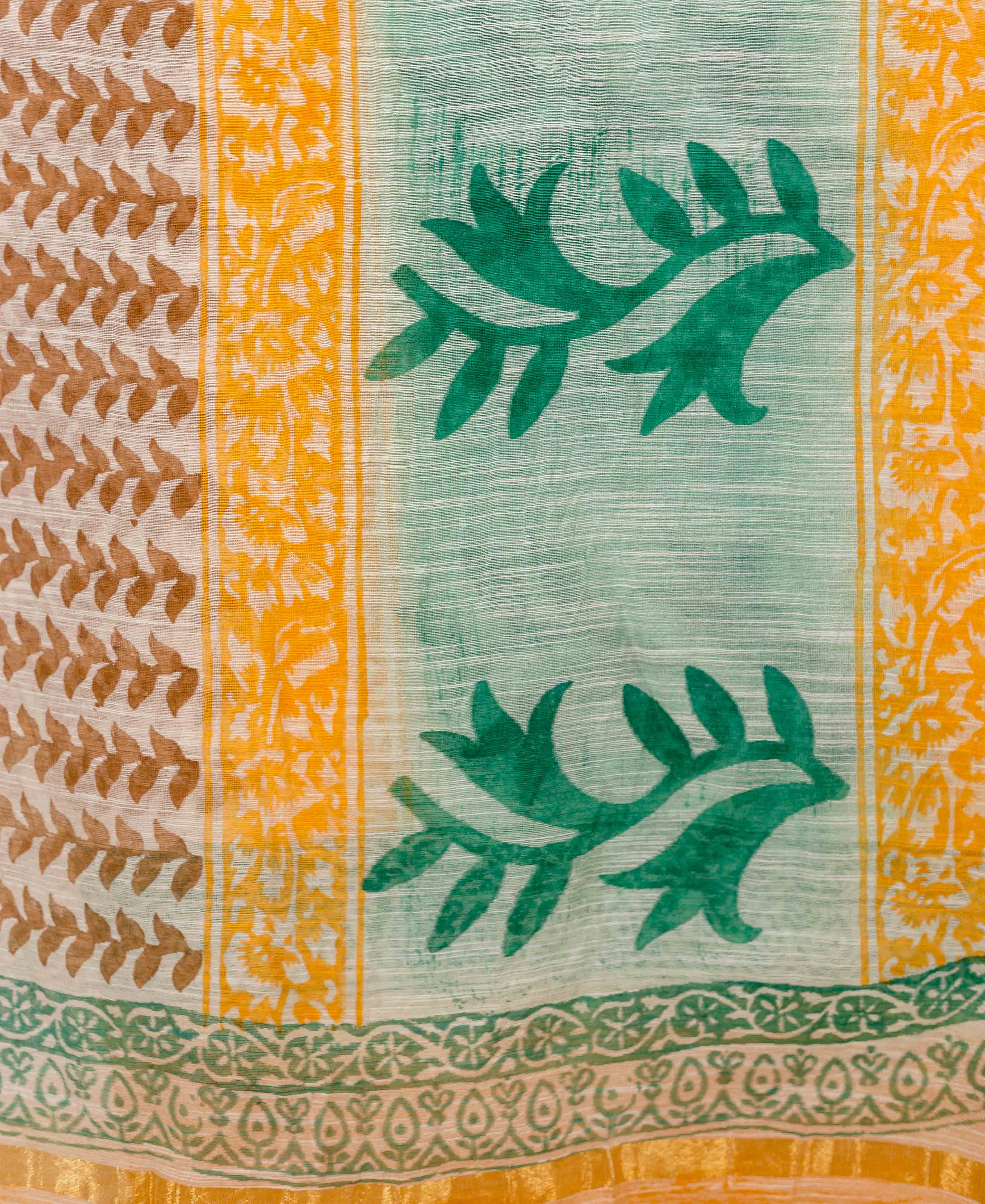 Detailed view of hand-block printed fabric with green, yellow, and brown botanical patterns.
