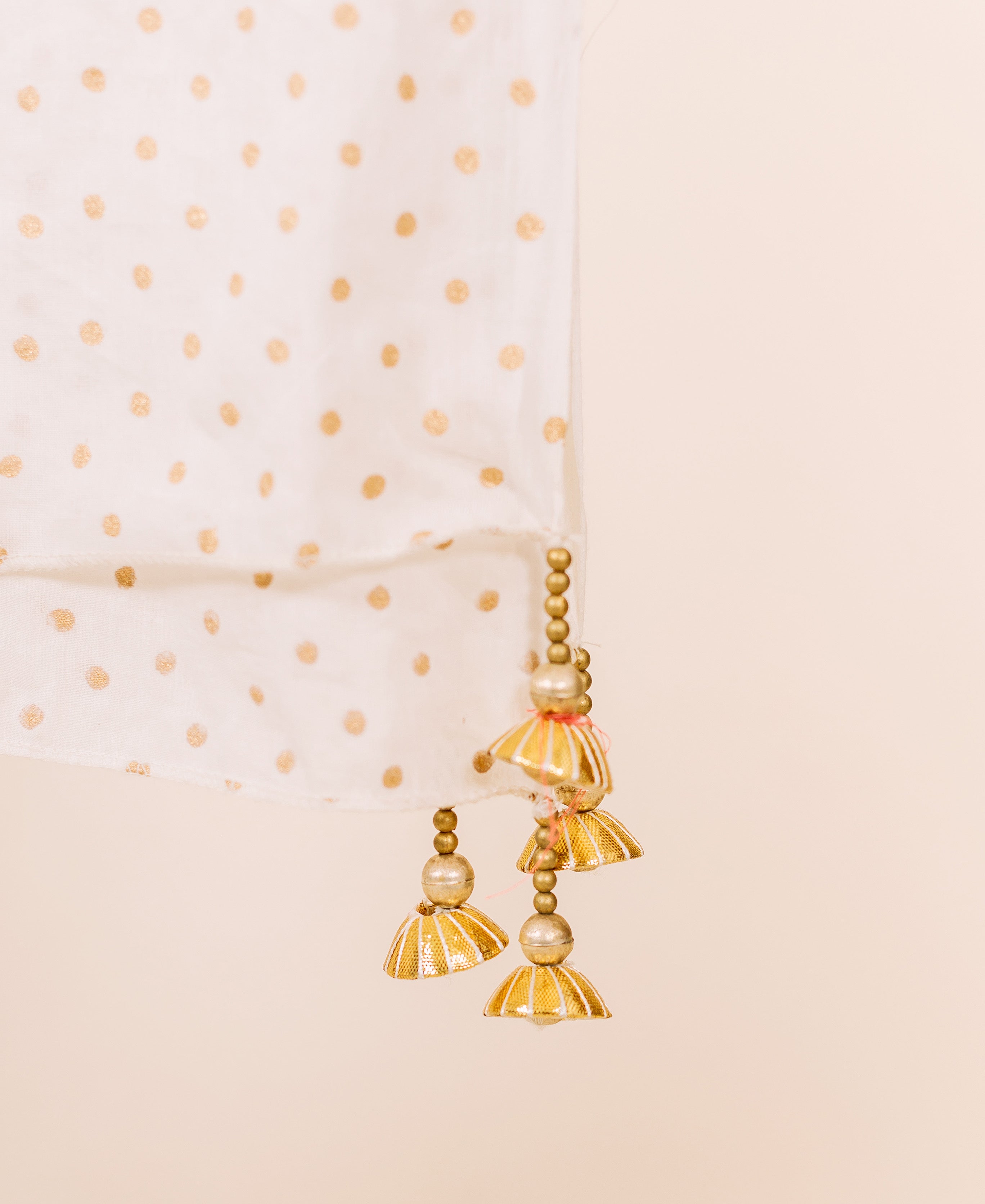 Draped white fabric with metallic gold polka dots, featuring ornate gold beaded tassels.
