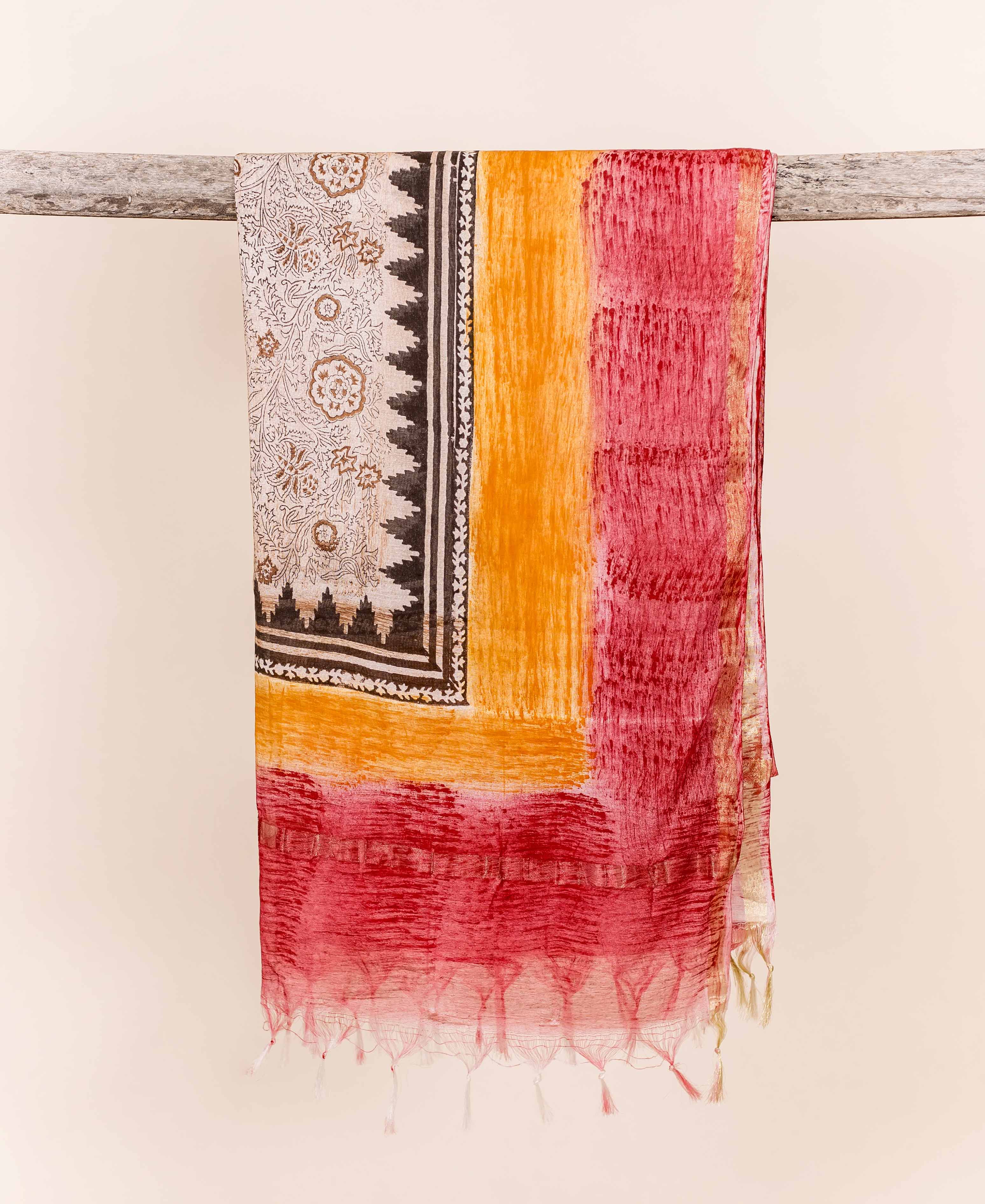 Vibrant red and orange dupatta with block print, textured dyes, and visible tassels, draped on wood.
