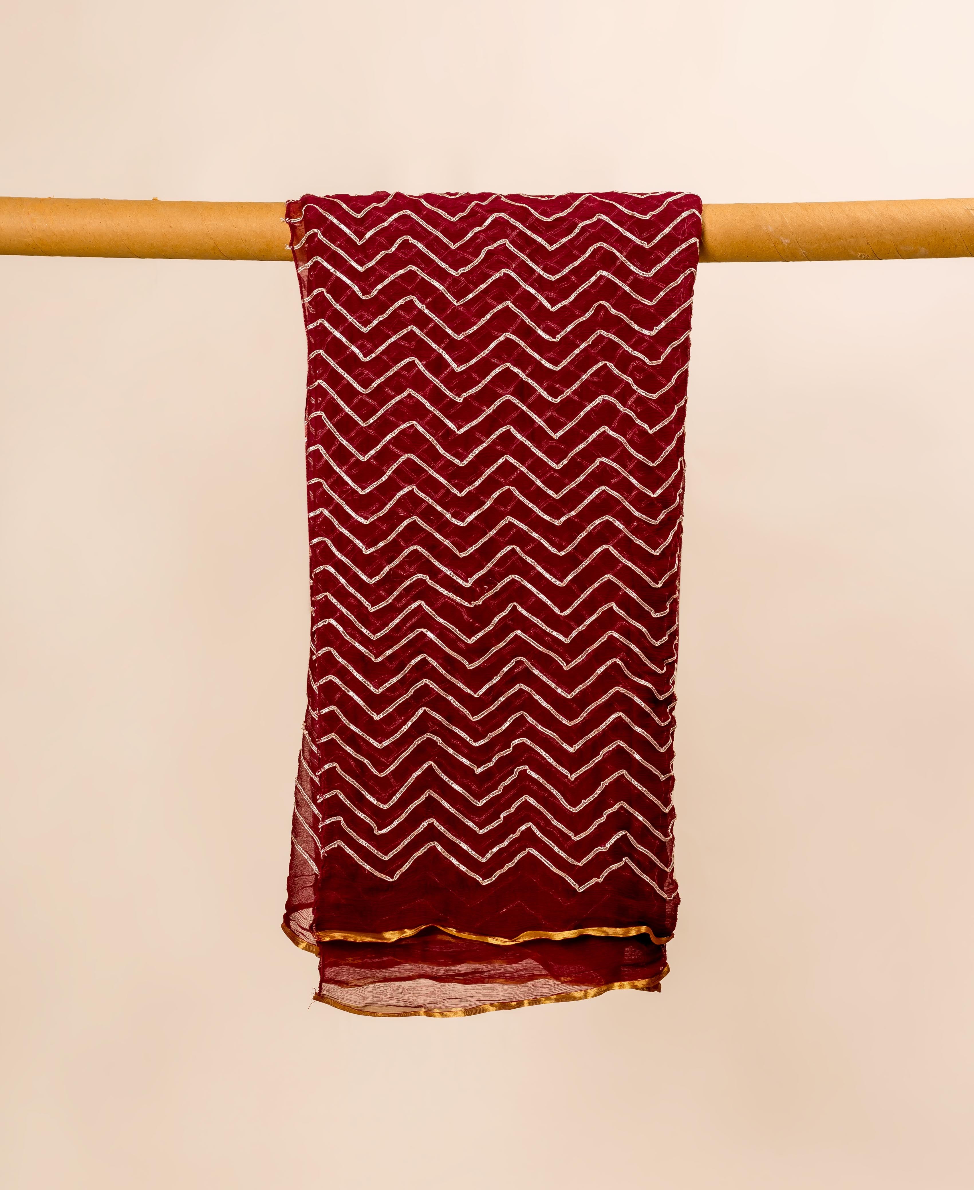 Maroon chiffon dupatta with white zigzag pattern and gold gotta detail, hanging.