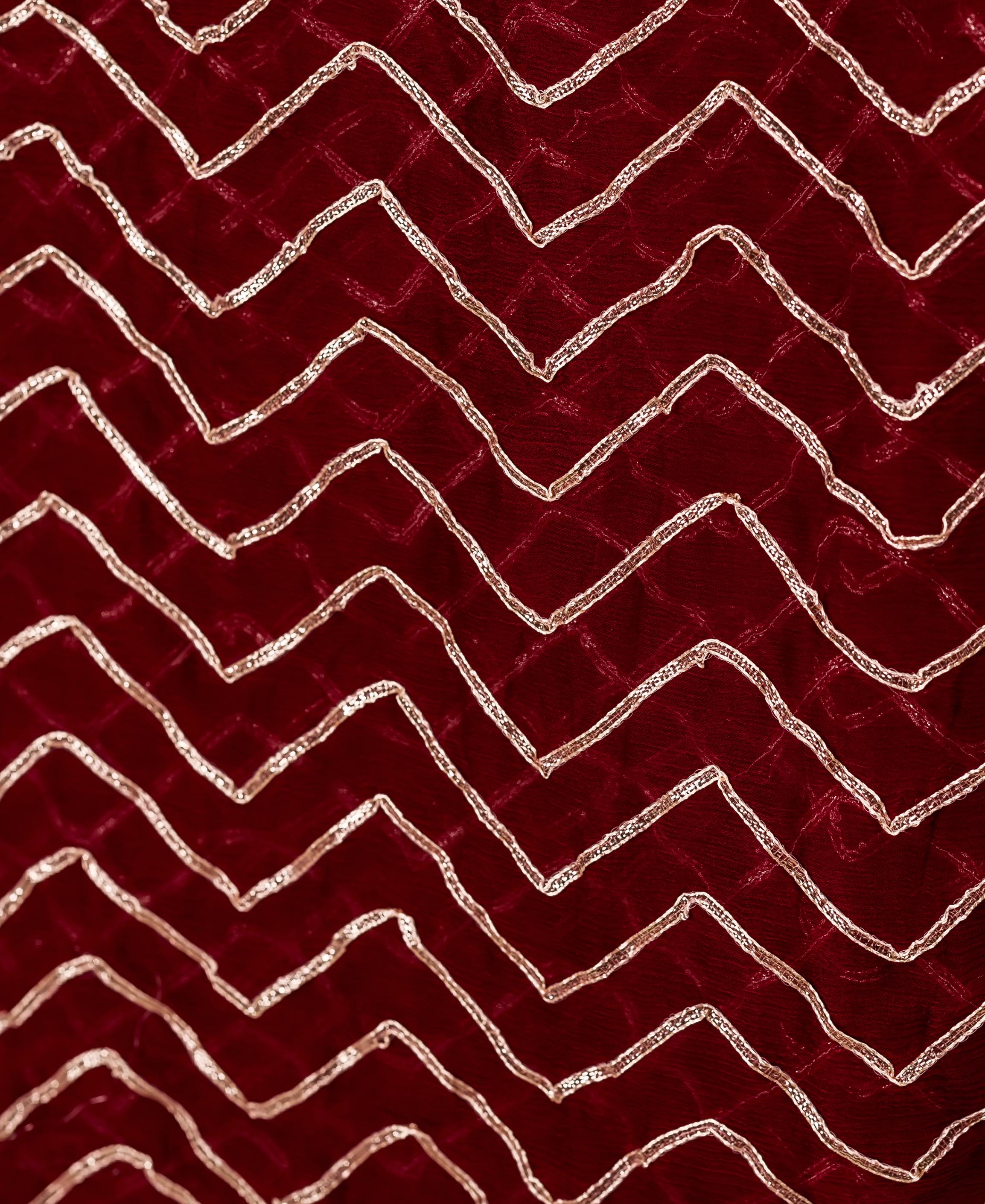 Close-up of maroon chiffon fabric with shimmering gold zigzag gotta pattern.
