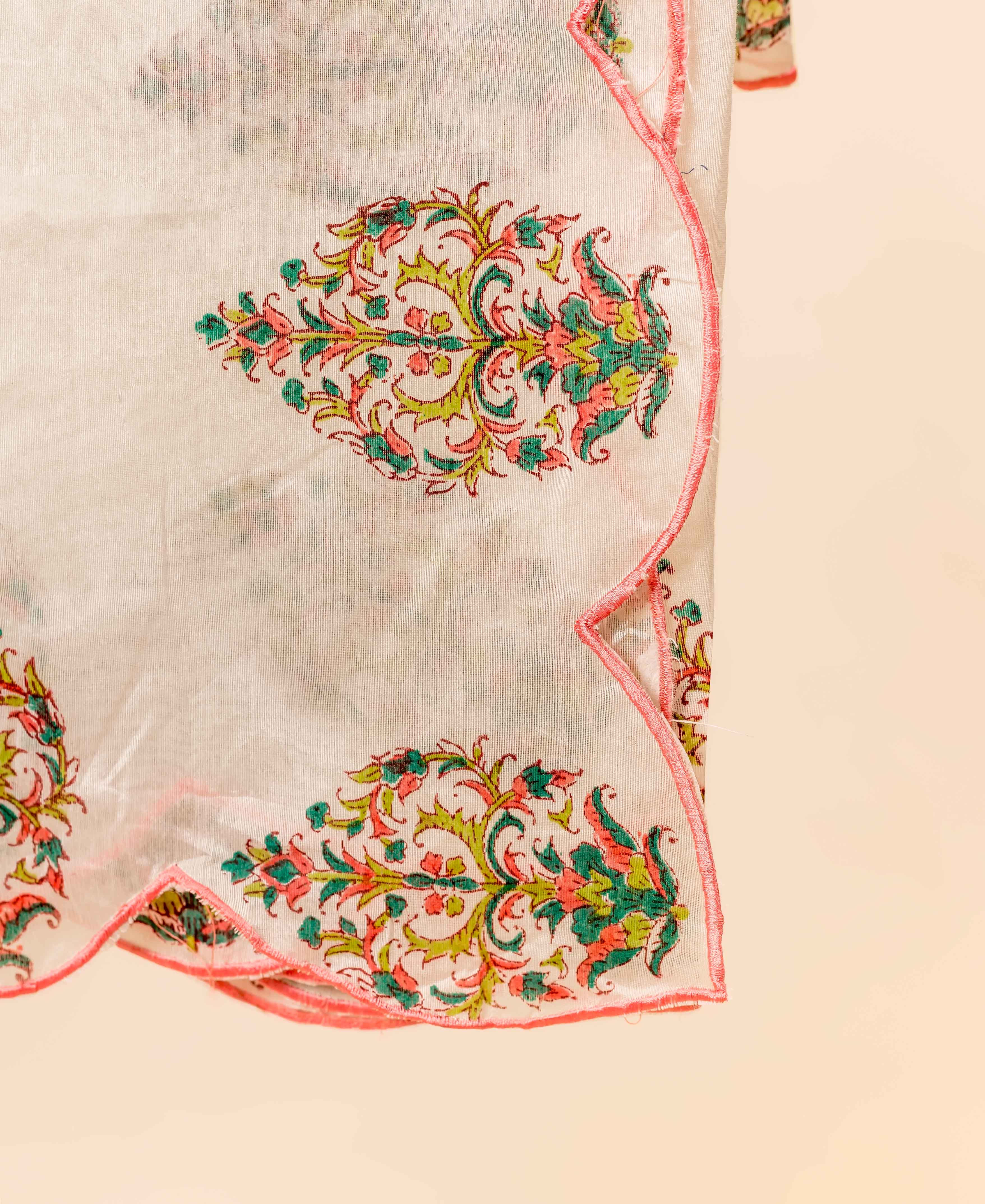 Close-up of white sheer fabric with pink and green floral block print, scalloped pink trim.