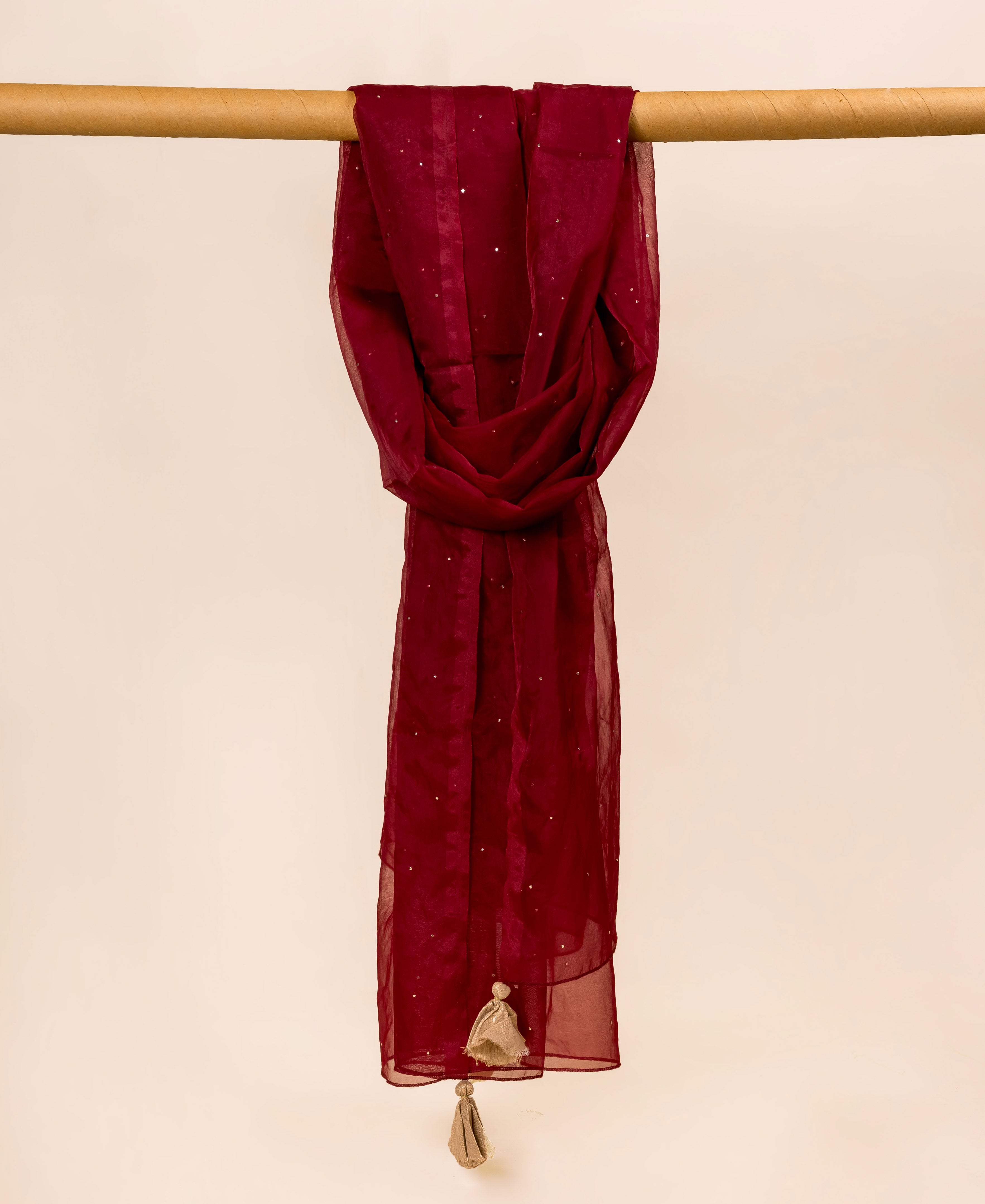Maroon organza dupatta with mukaish, draped over a wooden rod.